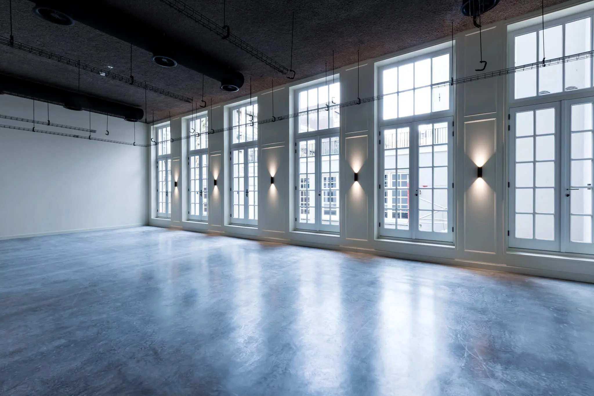 Lichte, lege ruimte met grote ramen aan de Overtoom in Amsterdam en een glanzende betonnen vloer.