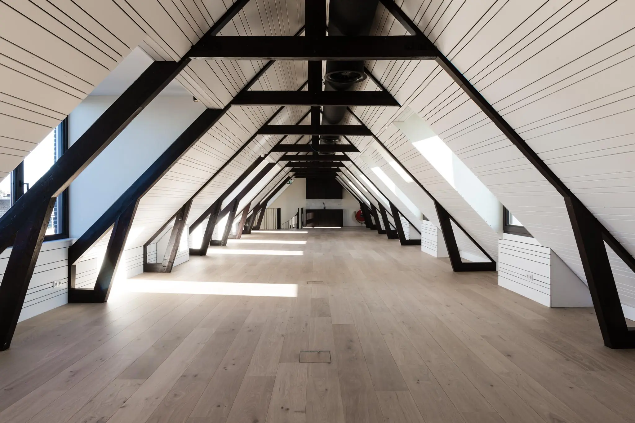 Ruim, gerenoveerd zolderinterieur aan de Overtoom met houten vloer, witte wanden en zwarte balkconstructie.