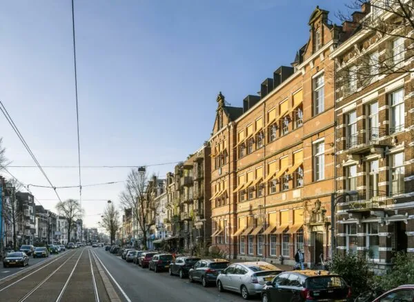 Straatbeeld van de Overtoom in Amsterdam met historische gevels, geparkeerde auto's en tramrails.