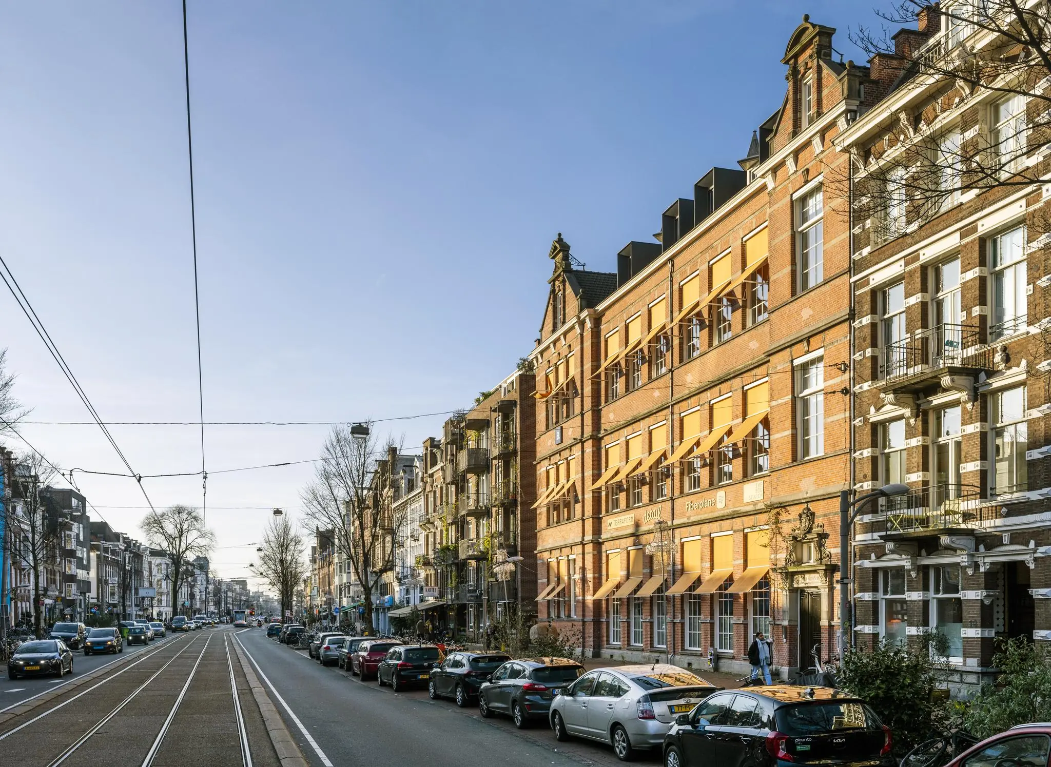 Straatbeeld van de Overtoom in Amsterdam met historische gevels, geparkeerde auto's en tramrails.