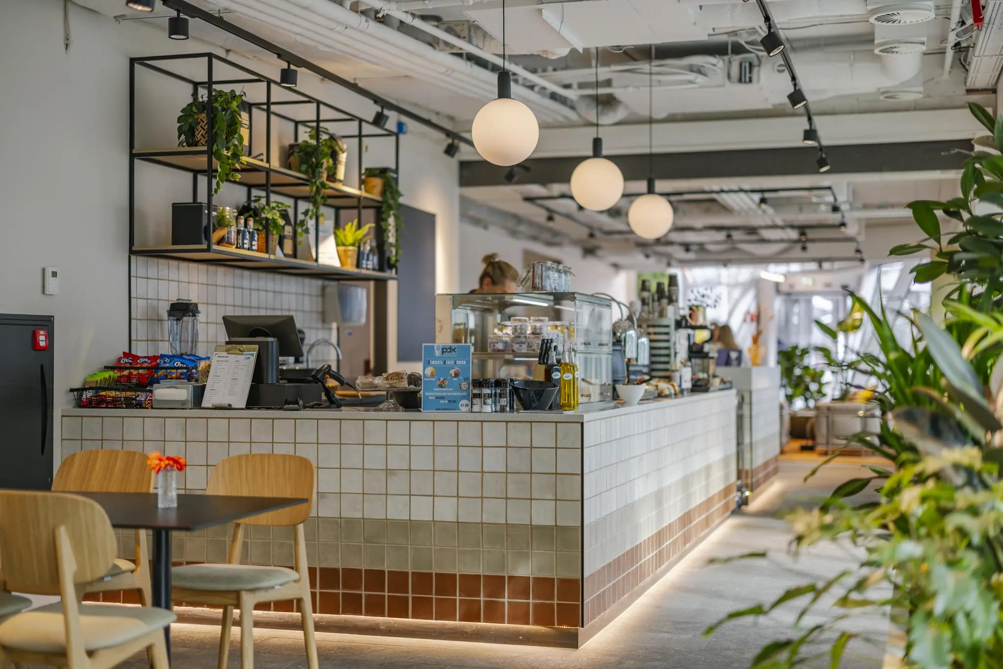 Moderne en sfeervol ingerichte koffiebar aan de Schenkkade met tegelcounter, hanglampen en veel planten.