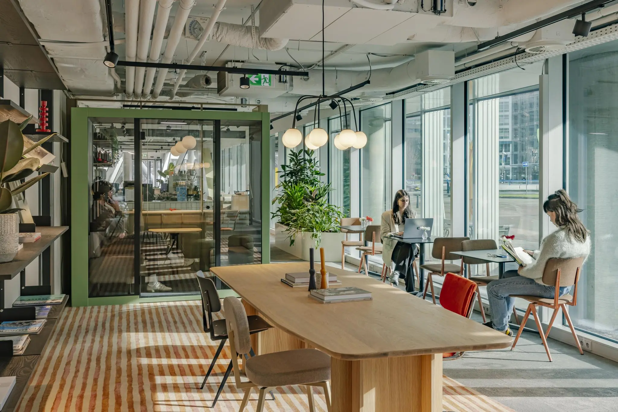 Moderne werkruimte aan de Schenkkade met grote ramen, houten meubilair en mensen die werken of lezen.