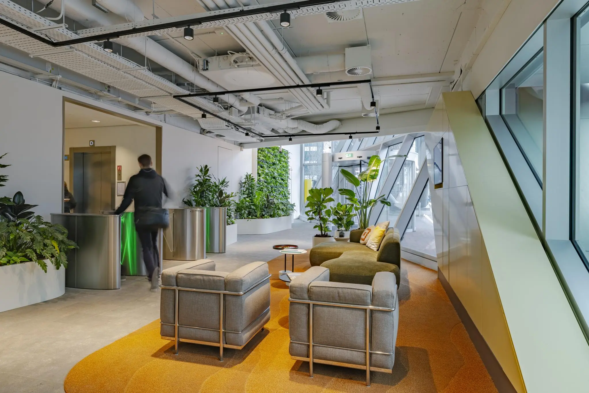 Moderne kantoorlobby aan de Schenkkade met loungezitjes, veel planten en een doorgang met toegangspoortjes.