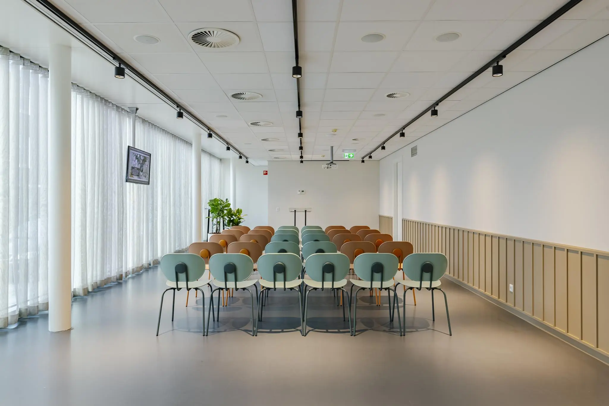 Moderne vergaderruimte aan de Schenkkade met kleurrijke stoelen, een katheder en natuurlijk licht via grote ramen.
