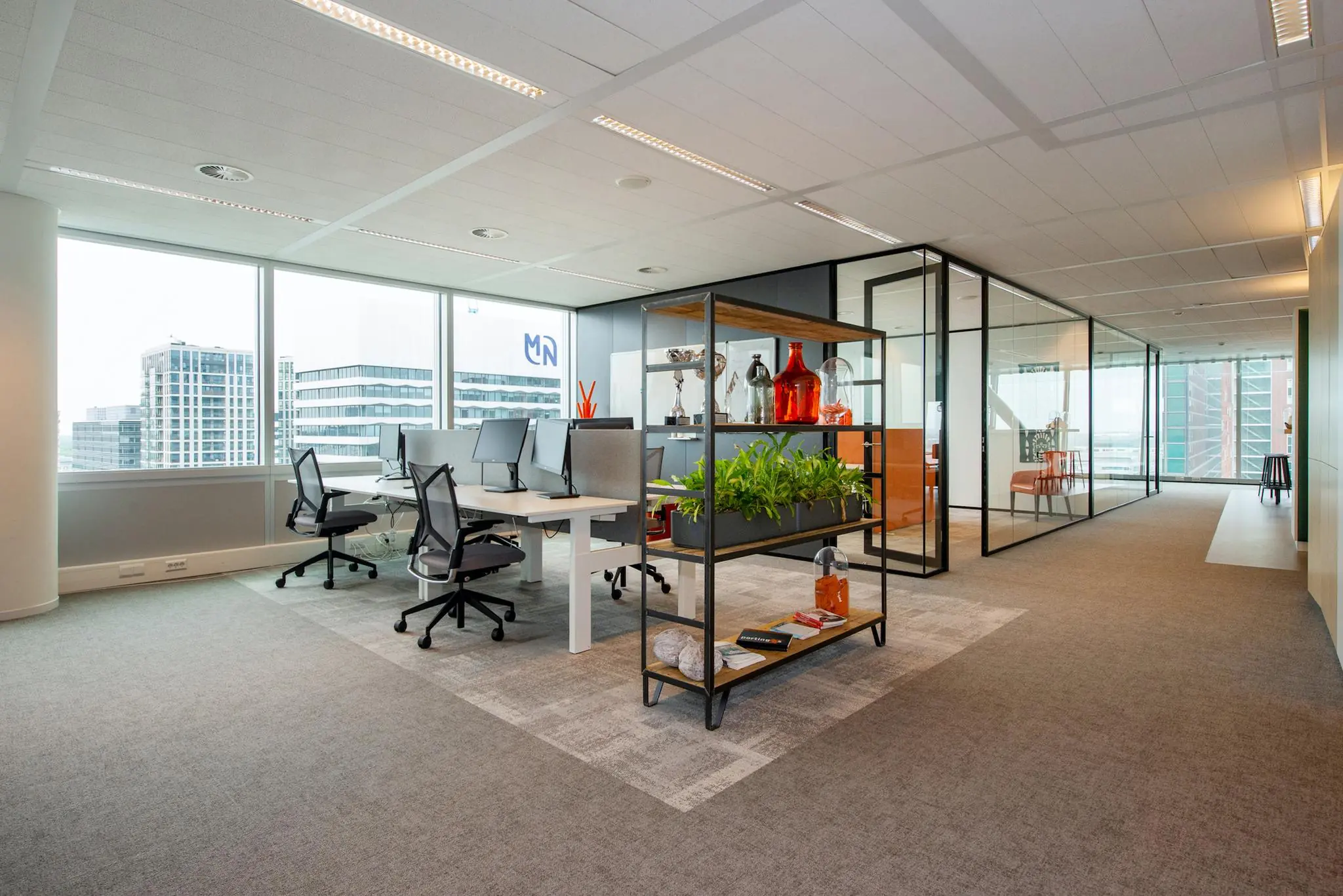 Modern kantoorinterieur aan de Schenkkade met open werkplekken, glazen vergaderruimtes en uitzicht op omliggende kantoorgebouwen.