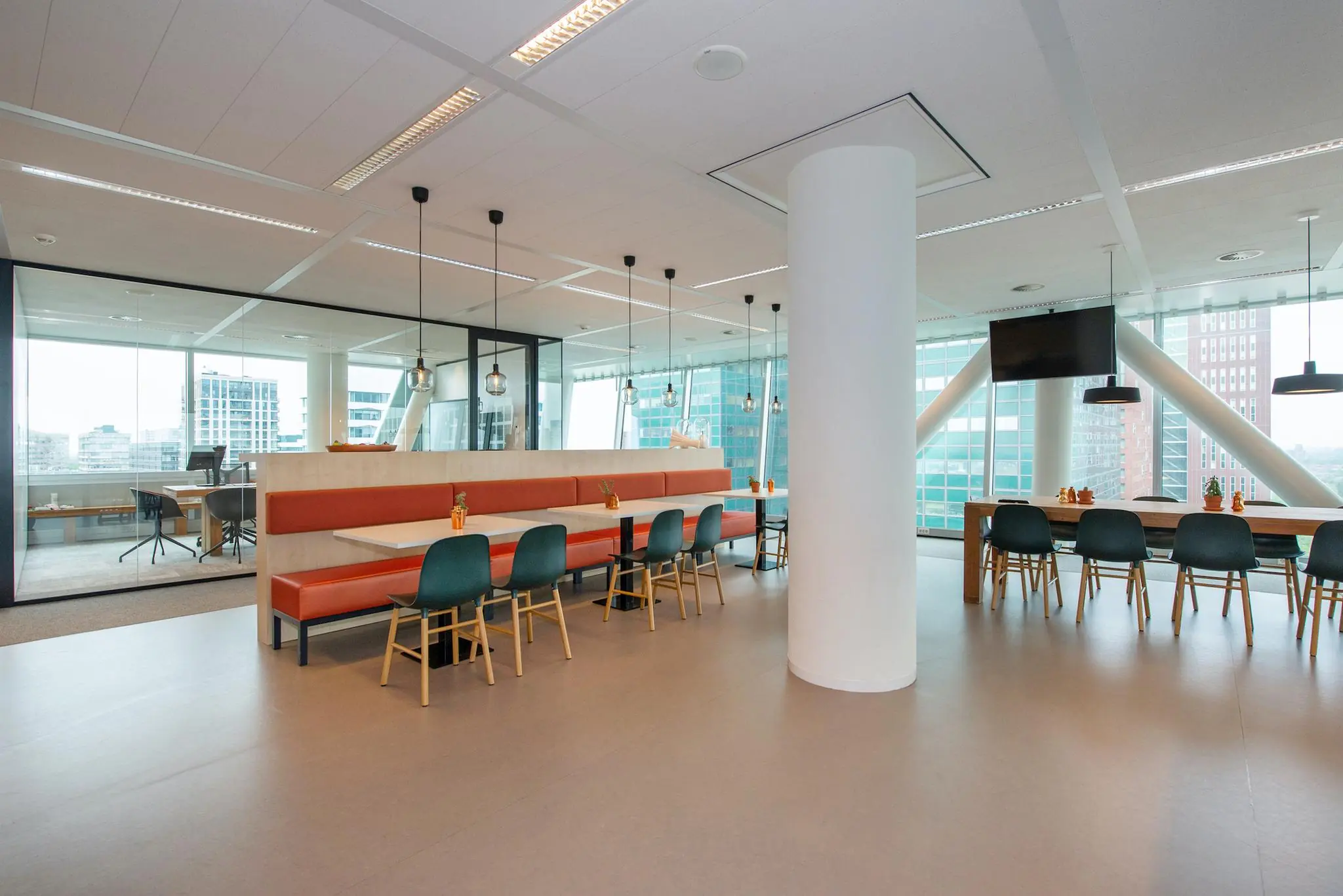 Moderne kantoorkantine aan de Schenkkade met lange eettafels, glazen wanden en uitzicht op omliggende kantoorgebouwen.