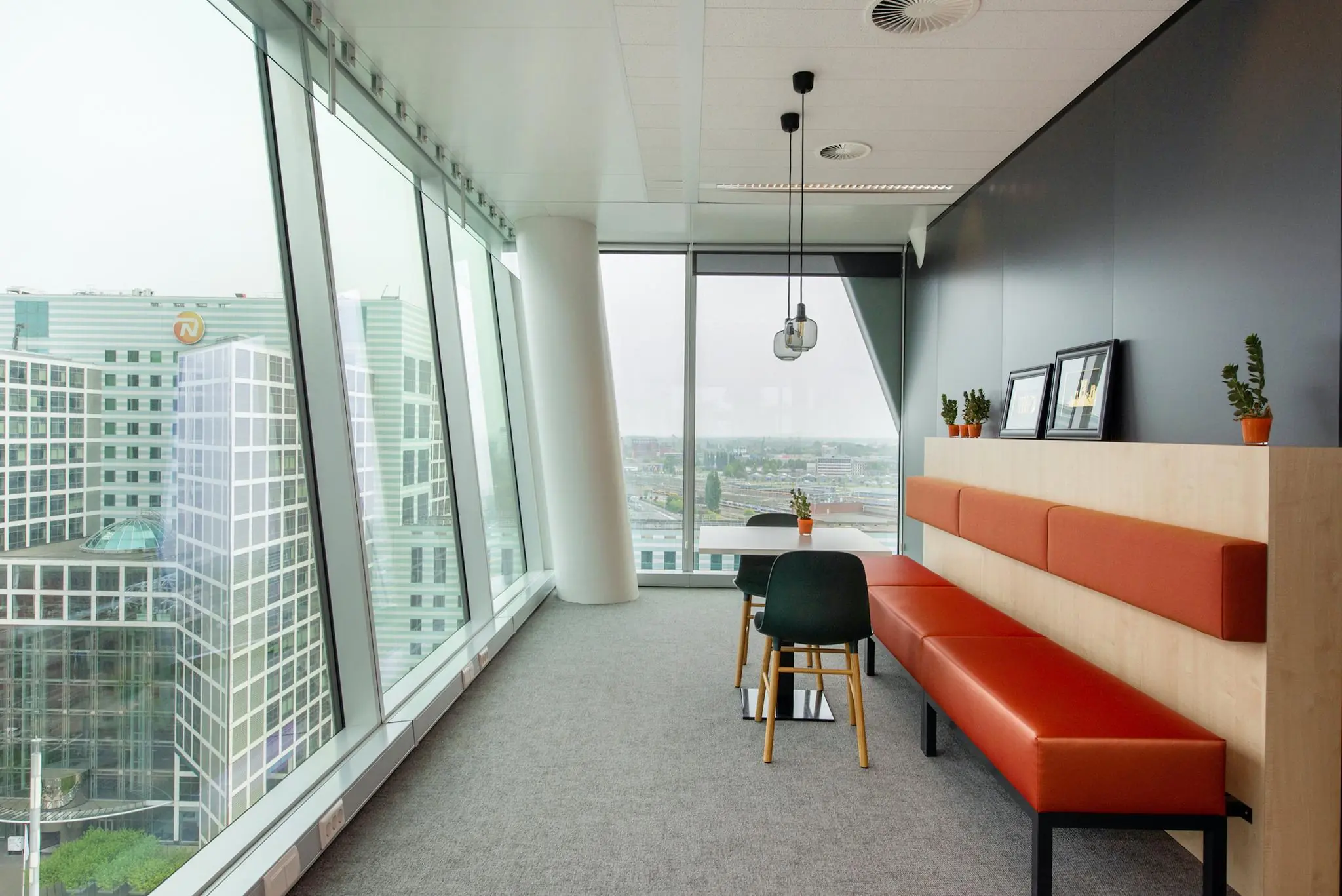Moderne kantoorruimte aan de Schenkkade met grote ramen, uitzicht op Den Haag en een zithoek met oranje bank en planten.
