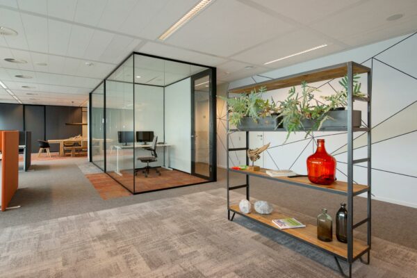 Modern kantoorinterieur aan de Schenkkade met glazen vergaderruimte, open werkplekken en een decoratief rek met planten en accessoires.
