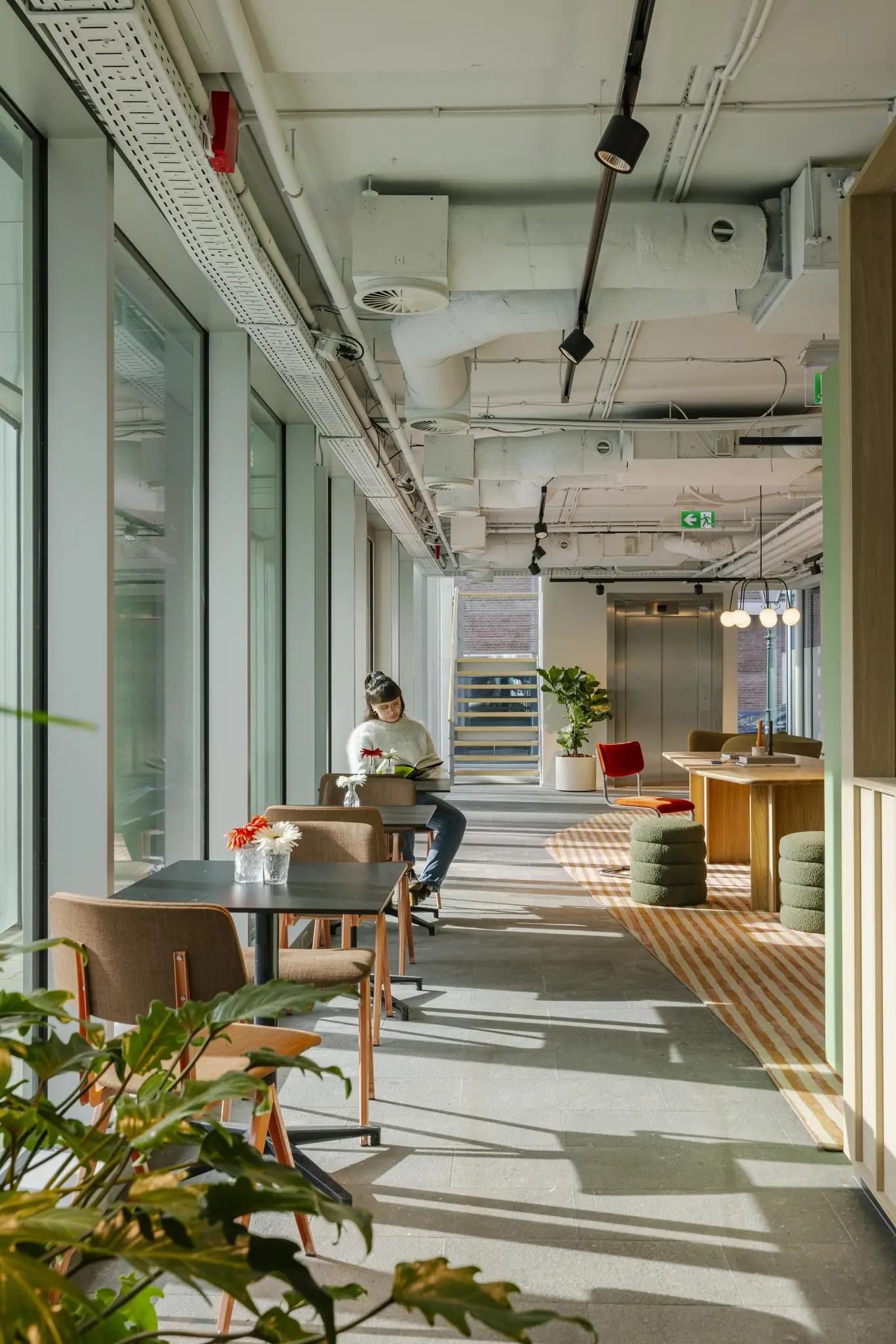 Moderne en lichte lounge- of werkruimte aan de Schenkkade met grote ramen, zitjes en een persoon die een boek leest.