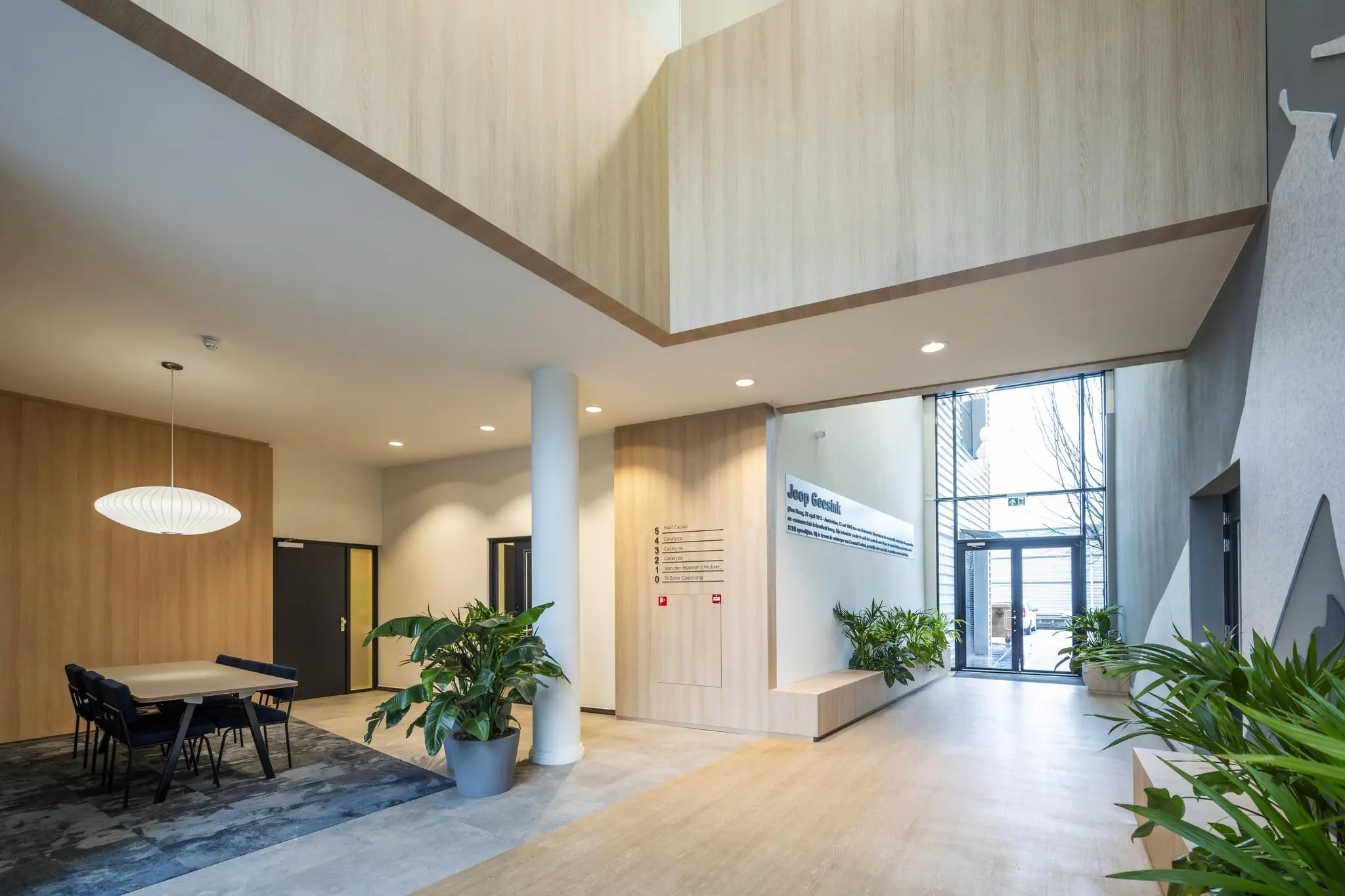 Moderne, lichte ontvangsthal aan de Joop Geesinkweg met houten accenten, zitgedeelte en veel groene planten.