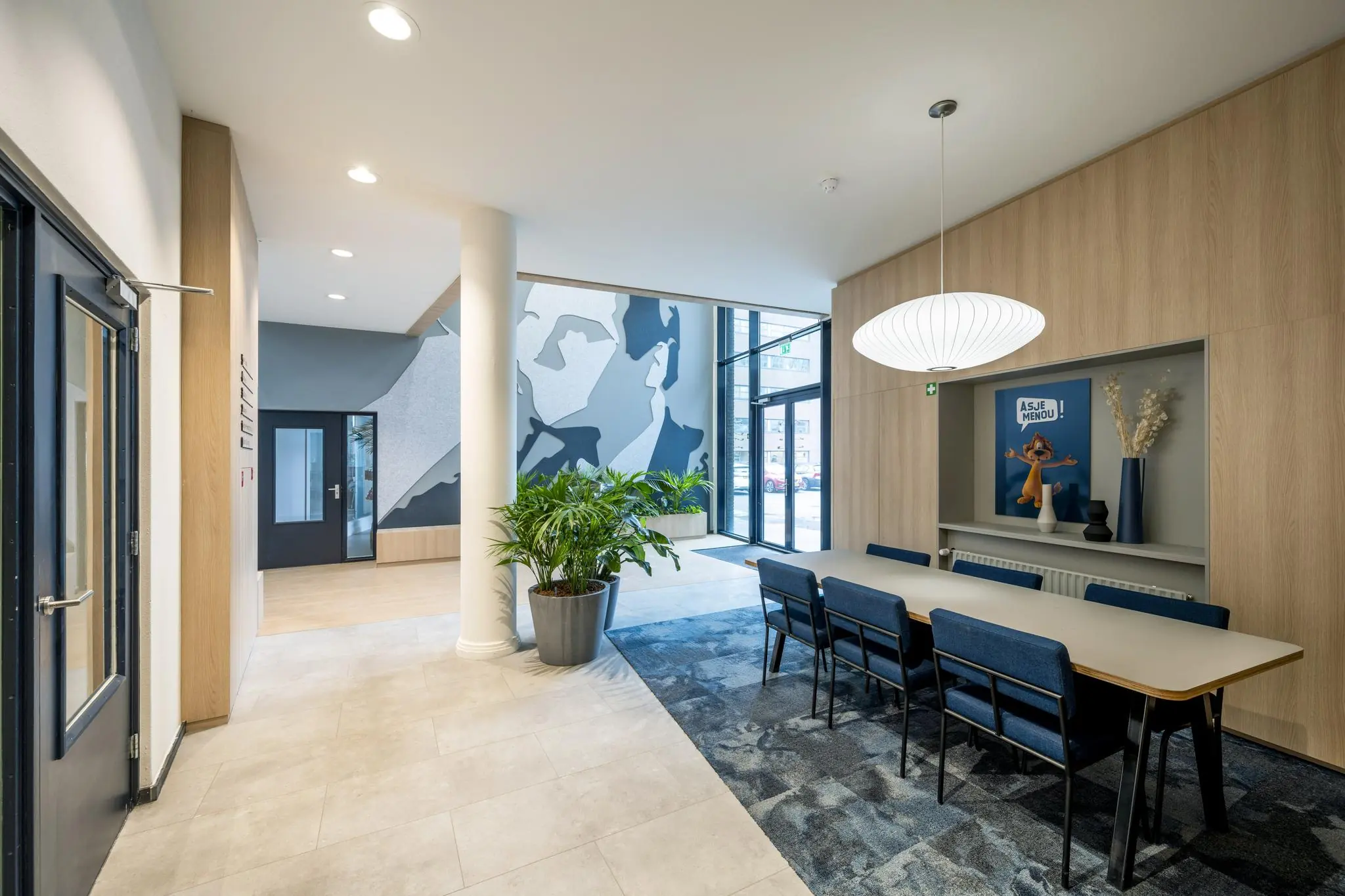 Moderne kantoorentree aan de Joop Geesinkweg met vergadertafel, grote muurschildering en decoratief nisje.