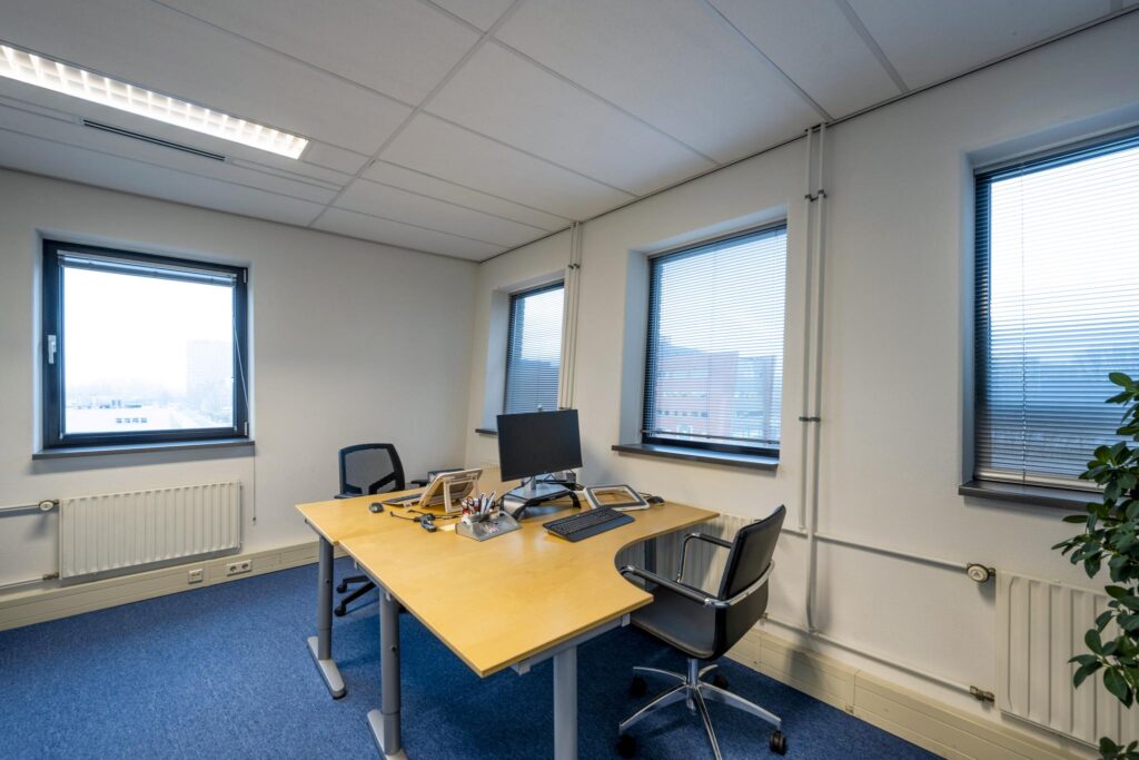 Modern ingericht kantoor met twee bureaustoelen, een bureau en drie ramen aan de Joop Geesinkweg.