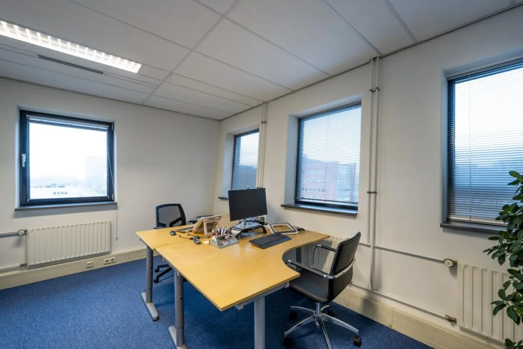 Modern ingericht kantoor met twee bureaustoelen, een bureau en drie ramen aan de Joop Geesinkweg.