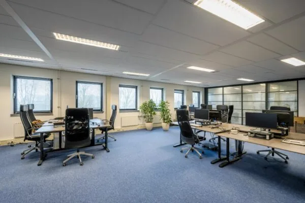 Ruim en modern kantoor aan de Joop Geesinkweg met meerdere bureaus, bureaustoelen, computers en grote ramen.