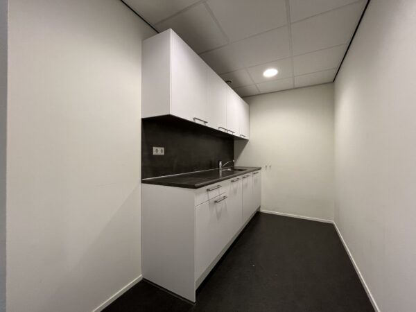 Kleine, smalle pantry-keuken met witte kasten, zwart werkblad en een ingebouwde spoelbak.
