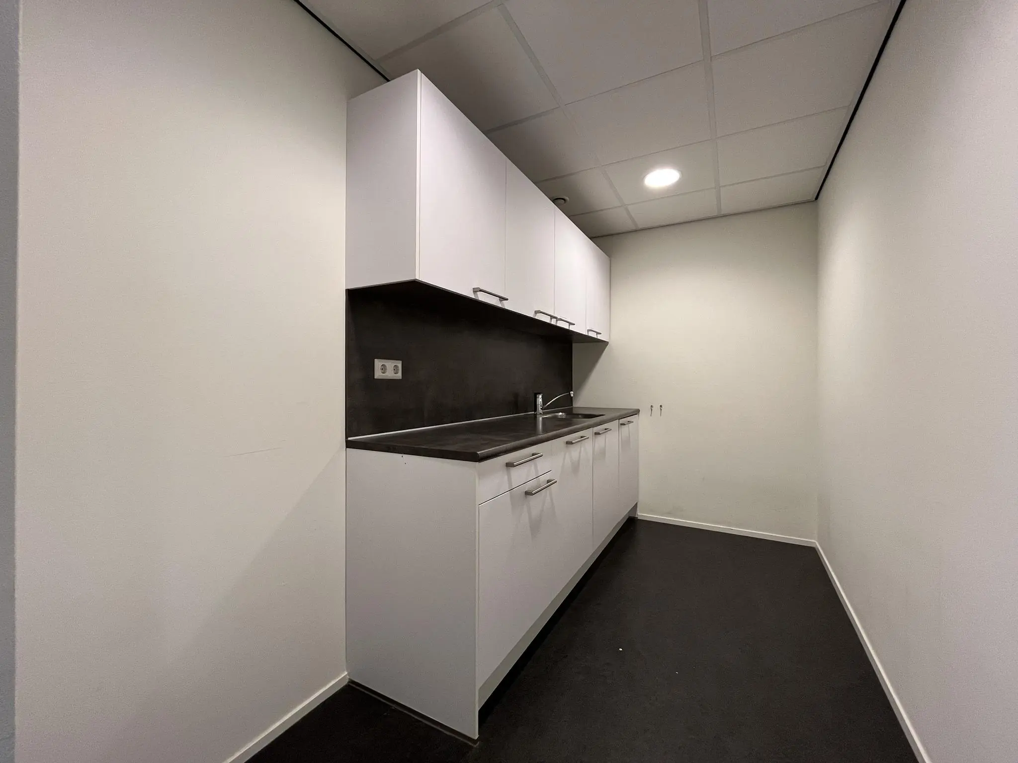 Kleine, smalle pantry-keuken met witte kasten, zwart werkblad en een ingebouwde spoelbak.