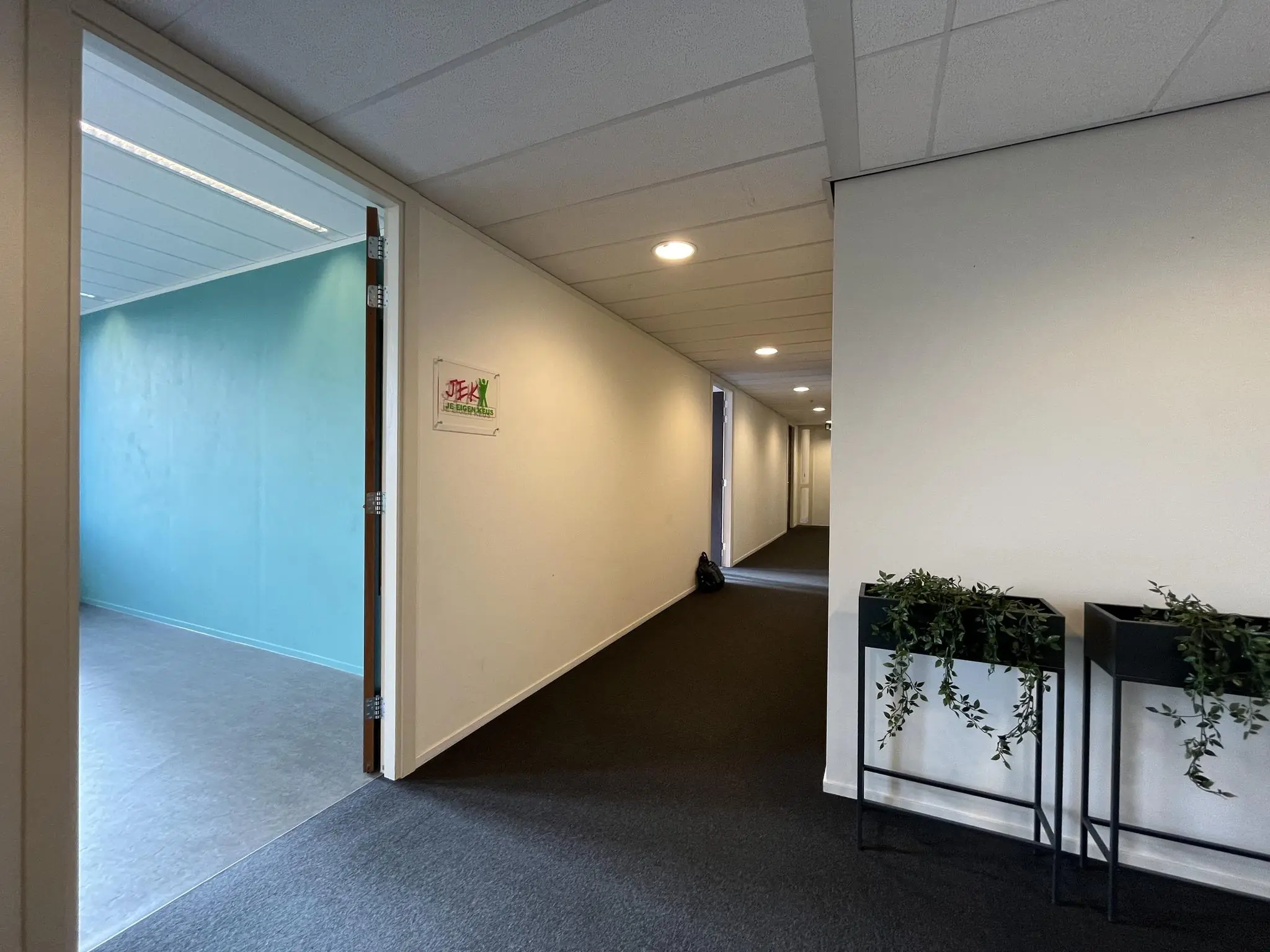 Hal met open deur naar een kamer van Jongerencentrum De Ratelaar, met plantenbakken aan de muur.