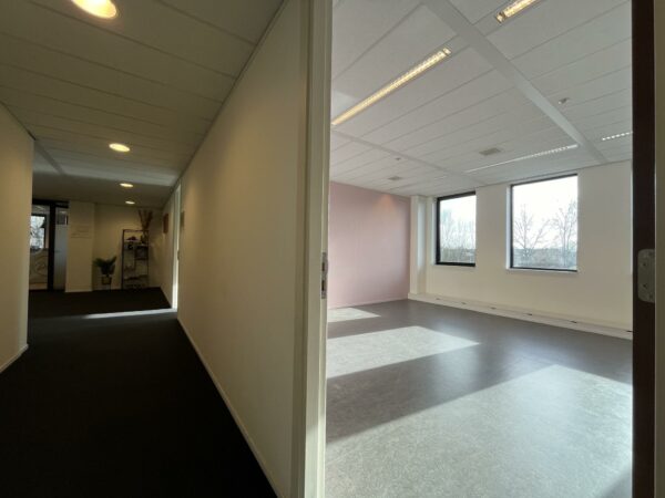 Zonnige, lege kantoorruimte met een lichtroze wand, gezien vanuit een gang in het gebouw Ratelaar.