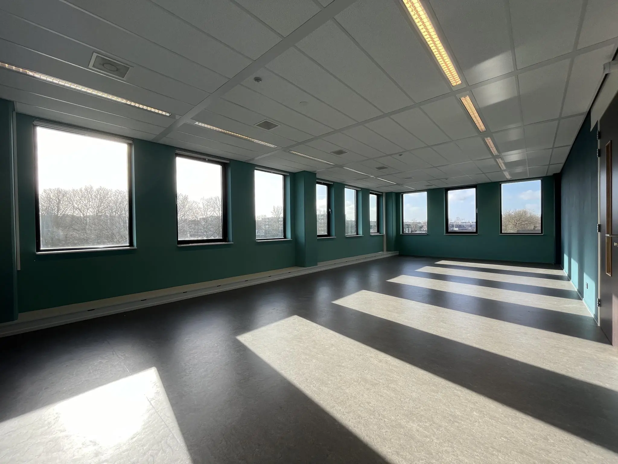 Lichte, lege kantoorruimte met turquoise muren en grote ramen in gebouw Ratelaar.