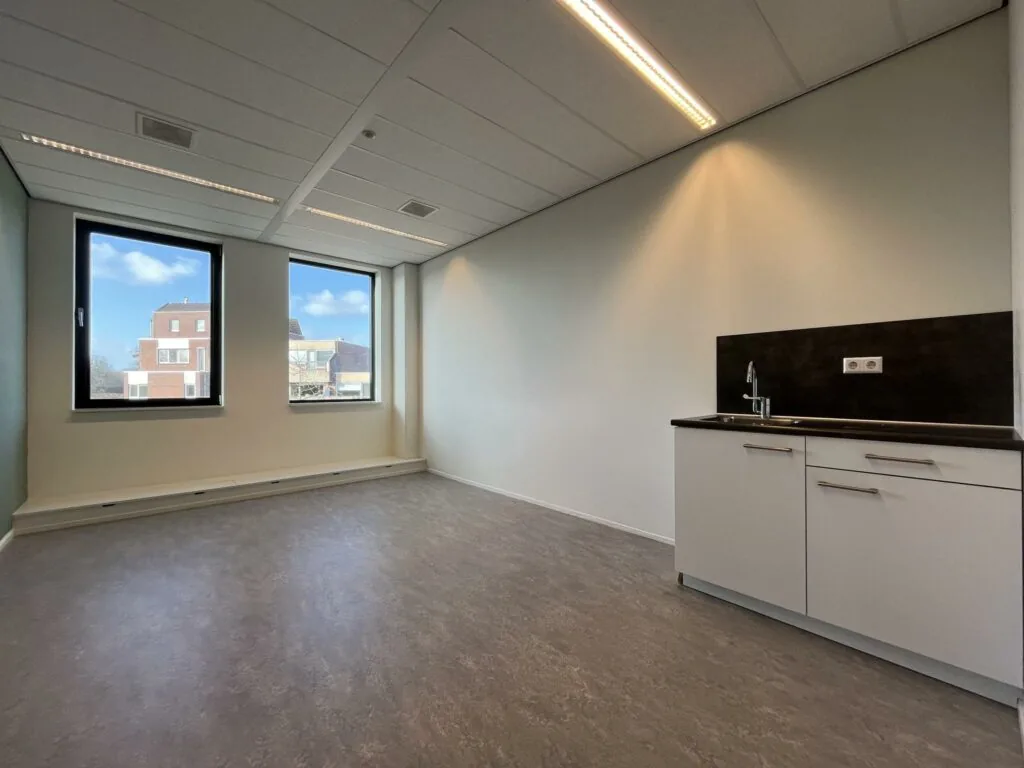 Licht en leeg kantoor met twee ramen en een wit keukenblok in gebouw Ratelaar.