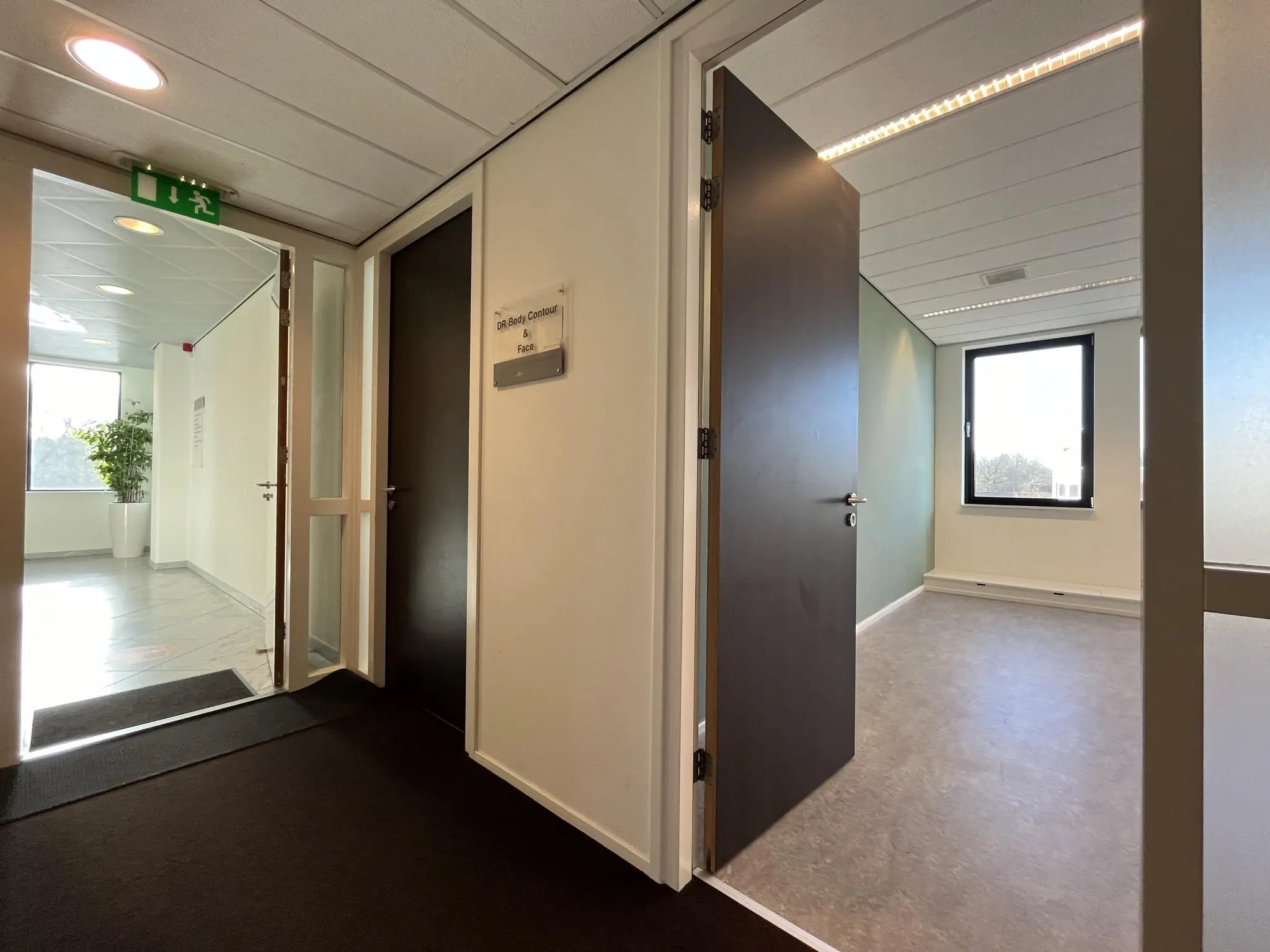 Hal van een modern kantoorpand met openstaande deuren naar een lege behandelkamer bij "DR. Body Contour & Face".
