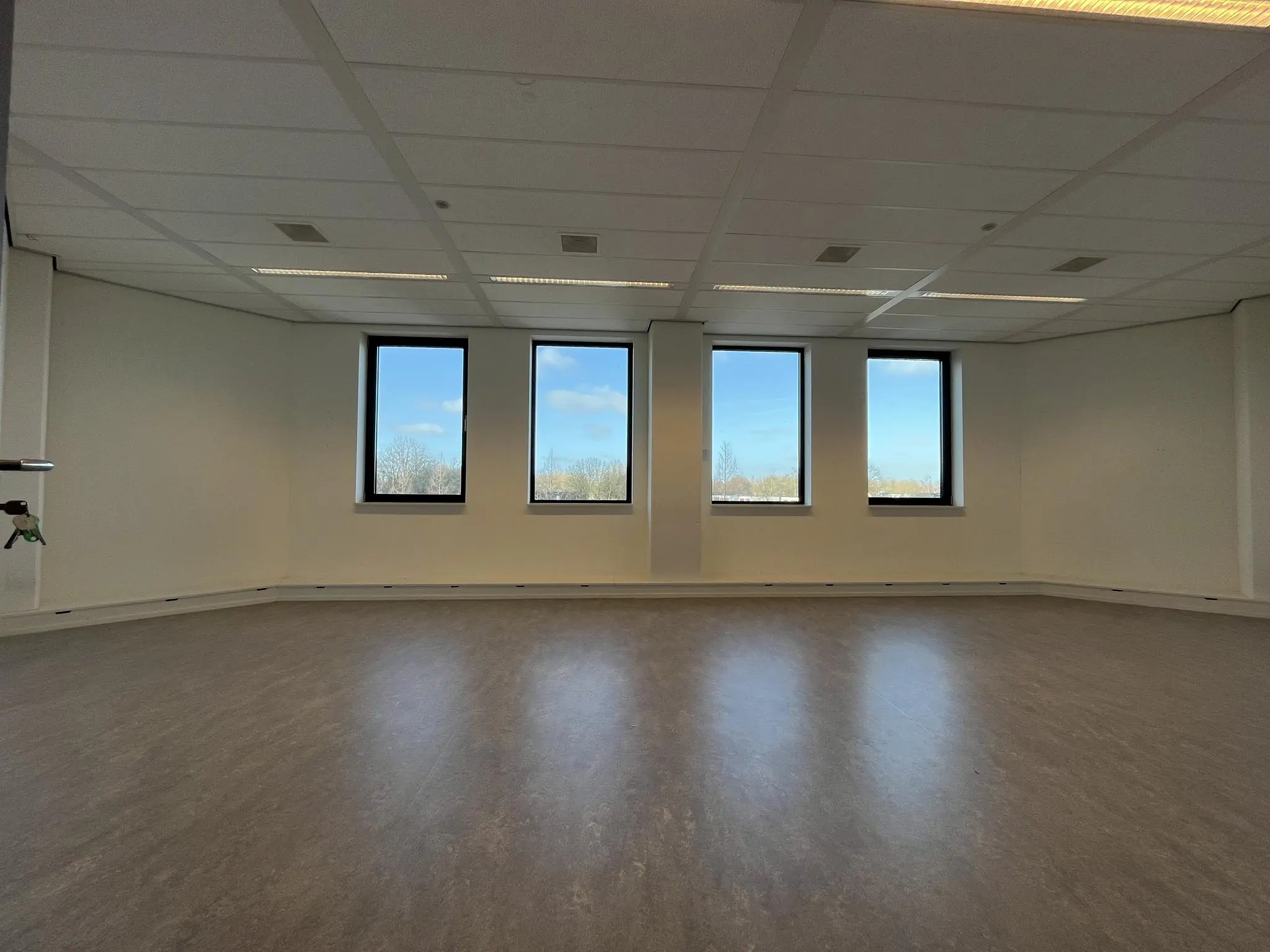 Lege kantoorruimte met vier ramen en uitzicht op een blauwe lucht bij Ratelaar.