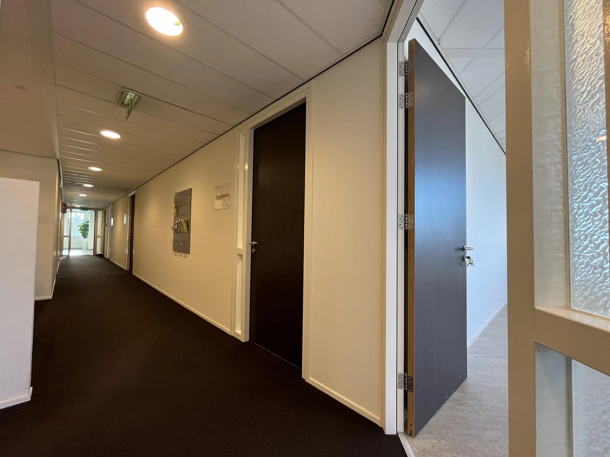 Een rustige kantoorhal met gesloten en één openstaande deur, waar een sleutel in het slot zit.