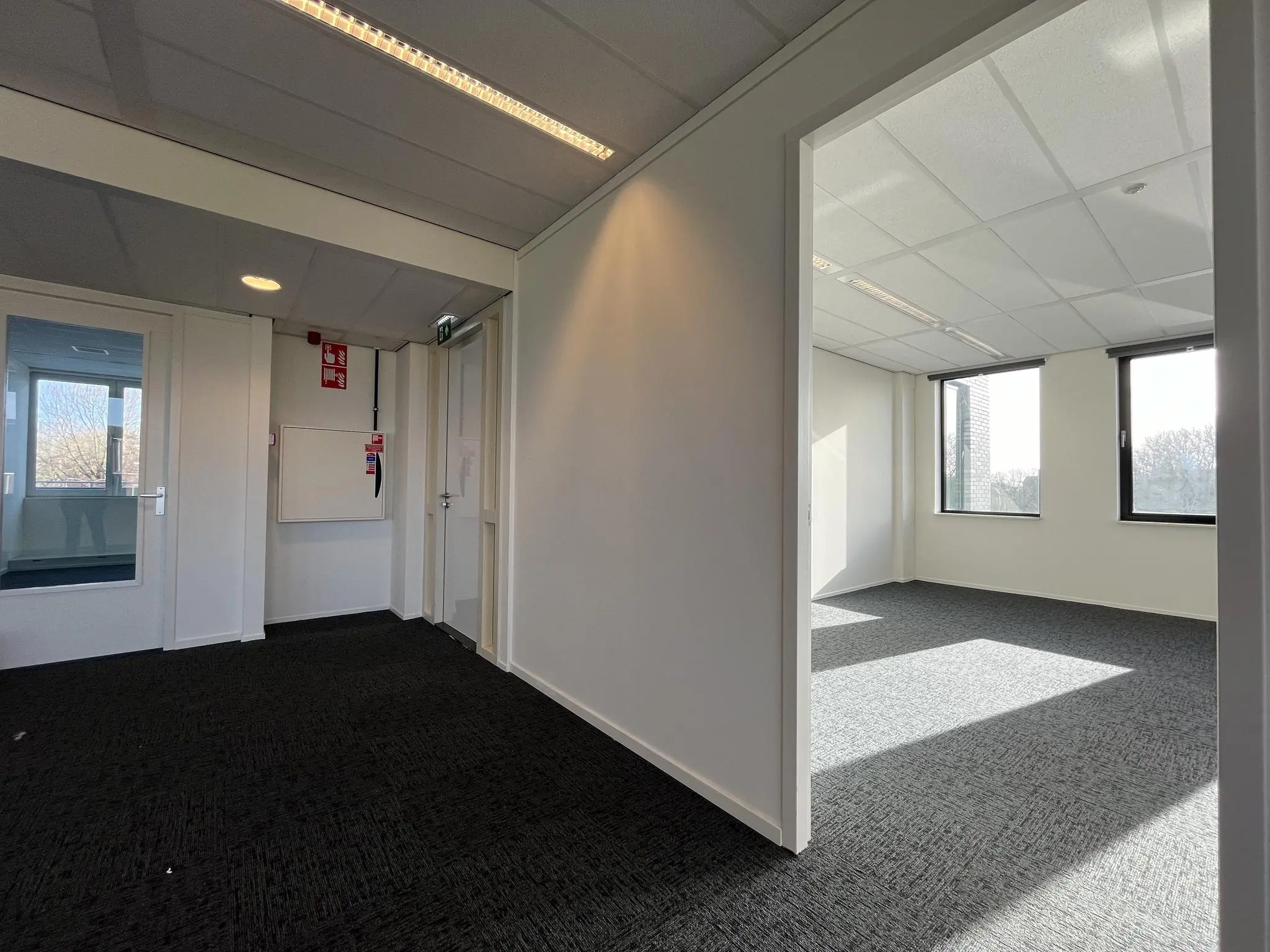 Lichte, lege kantoorruimte met ramen, grijze vloerbedekking en witte muren in gebouw Ratelaar.