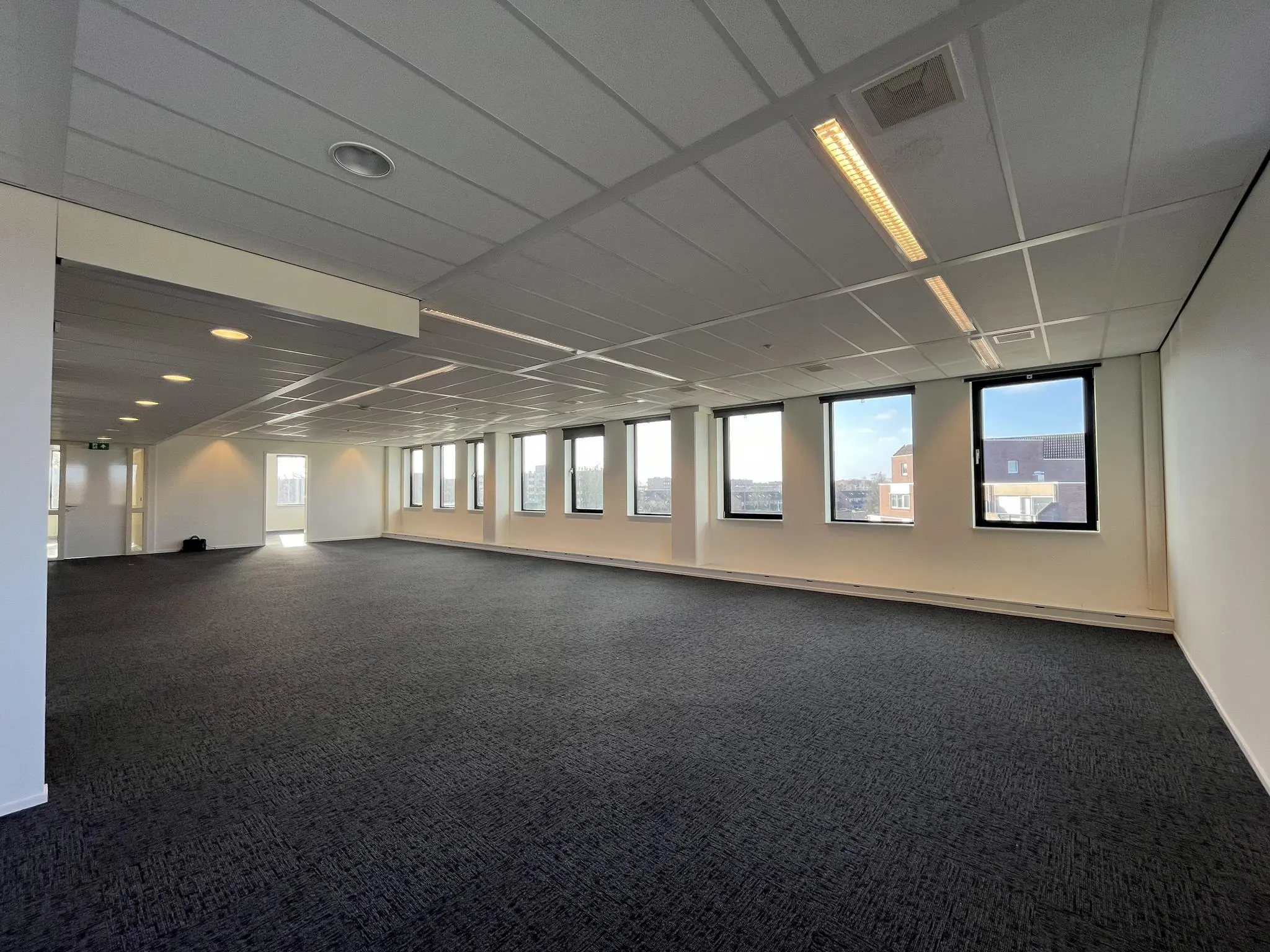 Ruime, lichte kantoorruimte in gebouw Ratelaar met blauw tapijt en grote ramen.