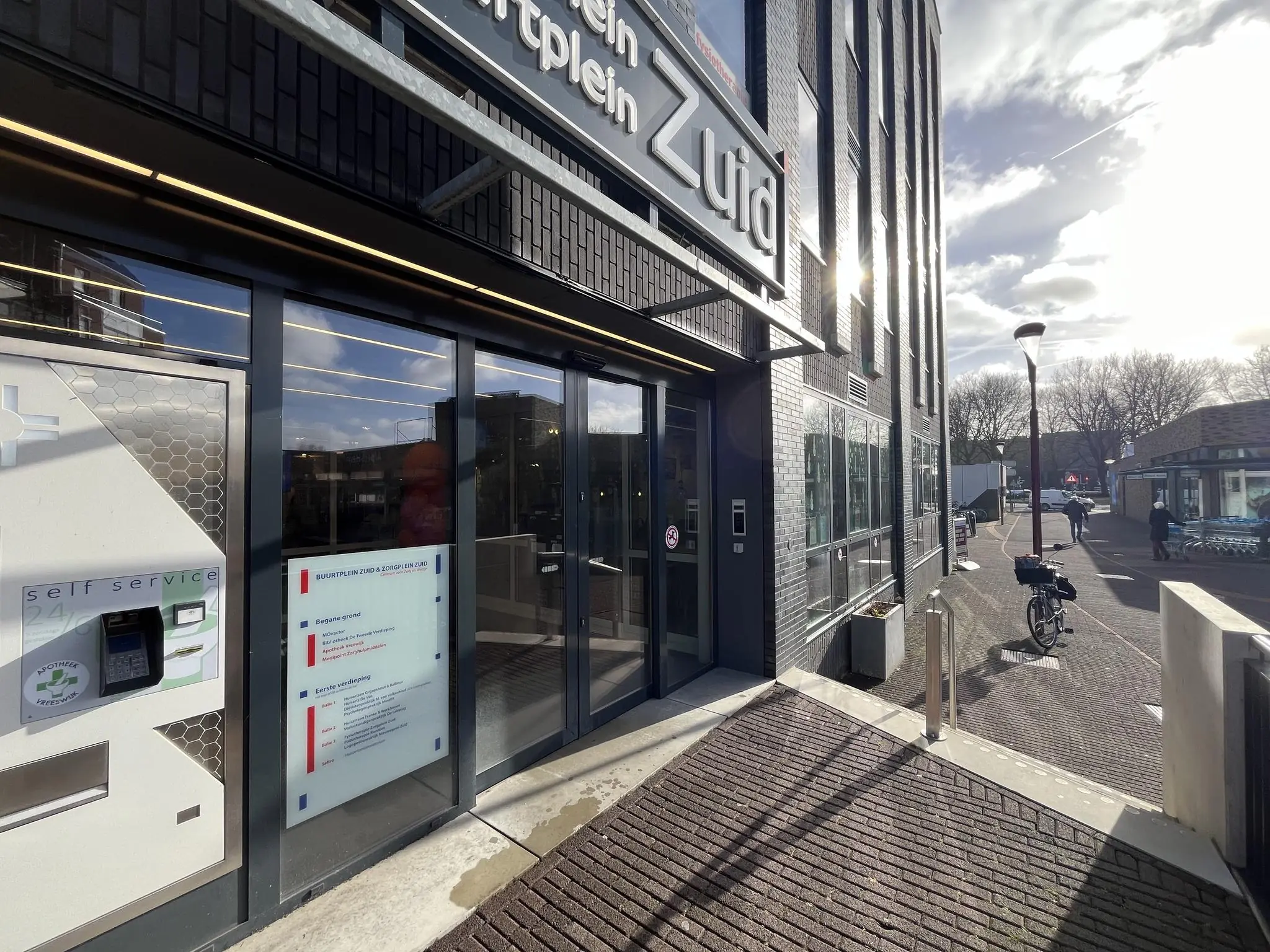 Ingang van Buurtplein Zuid met een 24-uurs afhaalautomaat van de apotheek aan de gevel.