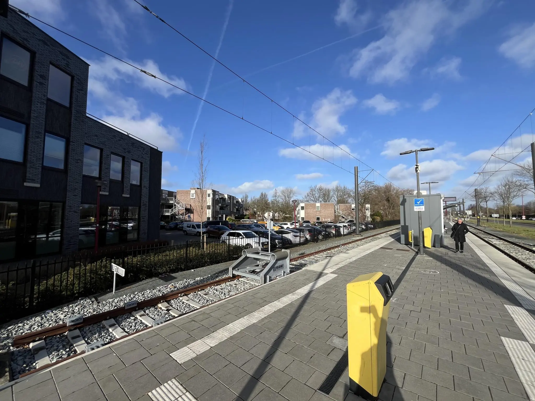Tramhalte Ratelaar met perrons, OV-chipkaartpalen en omliggende bebouwing op een zonnige dag.