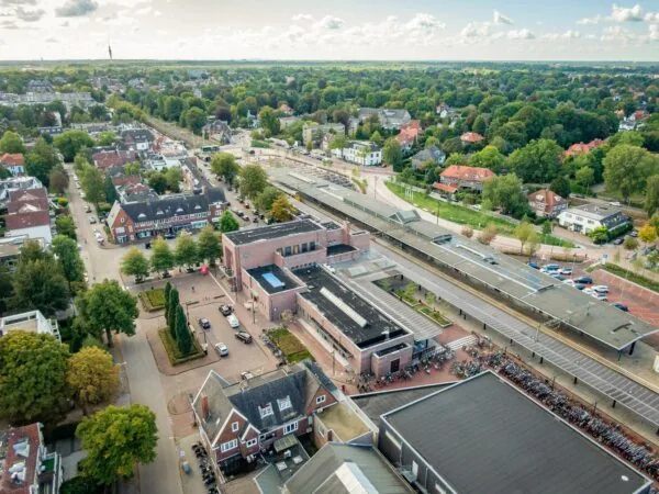 Luchtfoto van het Stationsplein in een groene woonwijk met het treinstation, fietsenstallingen en omliggende bebouwing.
