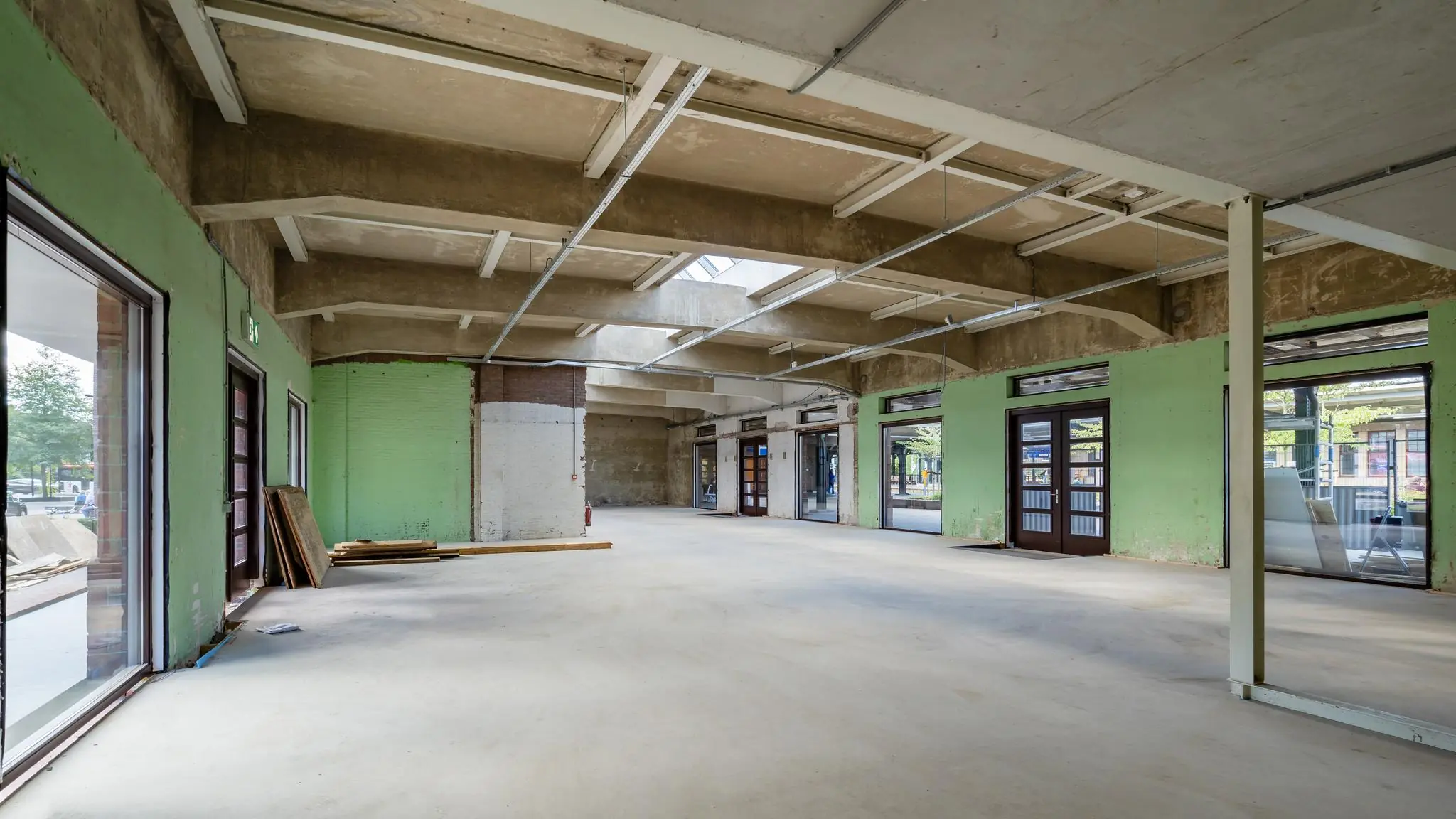 Leegstaand en deels gerenoveerd winkel- of kantoorpand aan het Stationsplein met zicht op grote ramen en betonnen plafond.