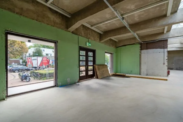 Binnenaanzicht van een lege, gedeeltelijk gerenoveerde ruimte aan het Stationsplein met uitzicht op een vrachtwagen van Zandbergen buiten.