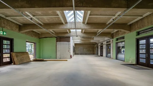 Leegstaande, industriële ruimte aan het Stationsplein met betonnen plafond, groene muren en grote ramen en deuren.