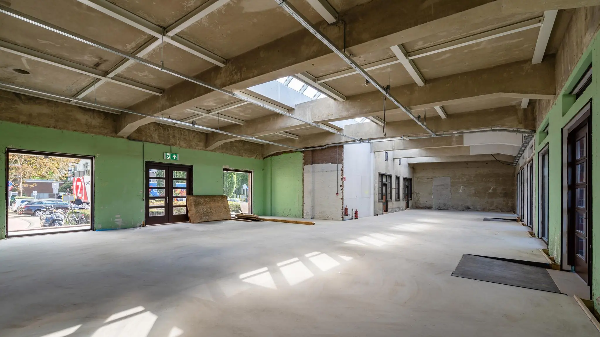 Leegstaand industrieel interieur van een gerenoveerd pand aan het Stationsplein met betonnen plafond en groen geverfde muren.
