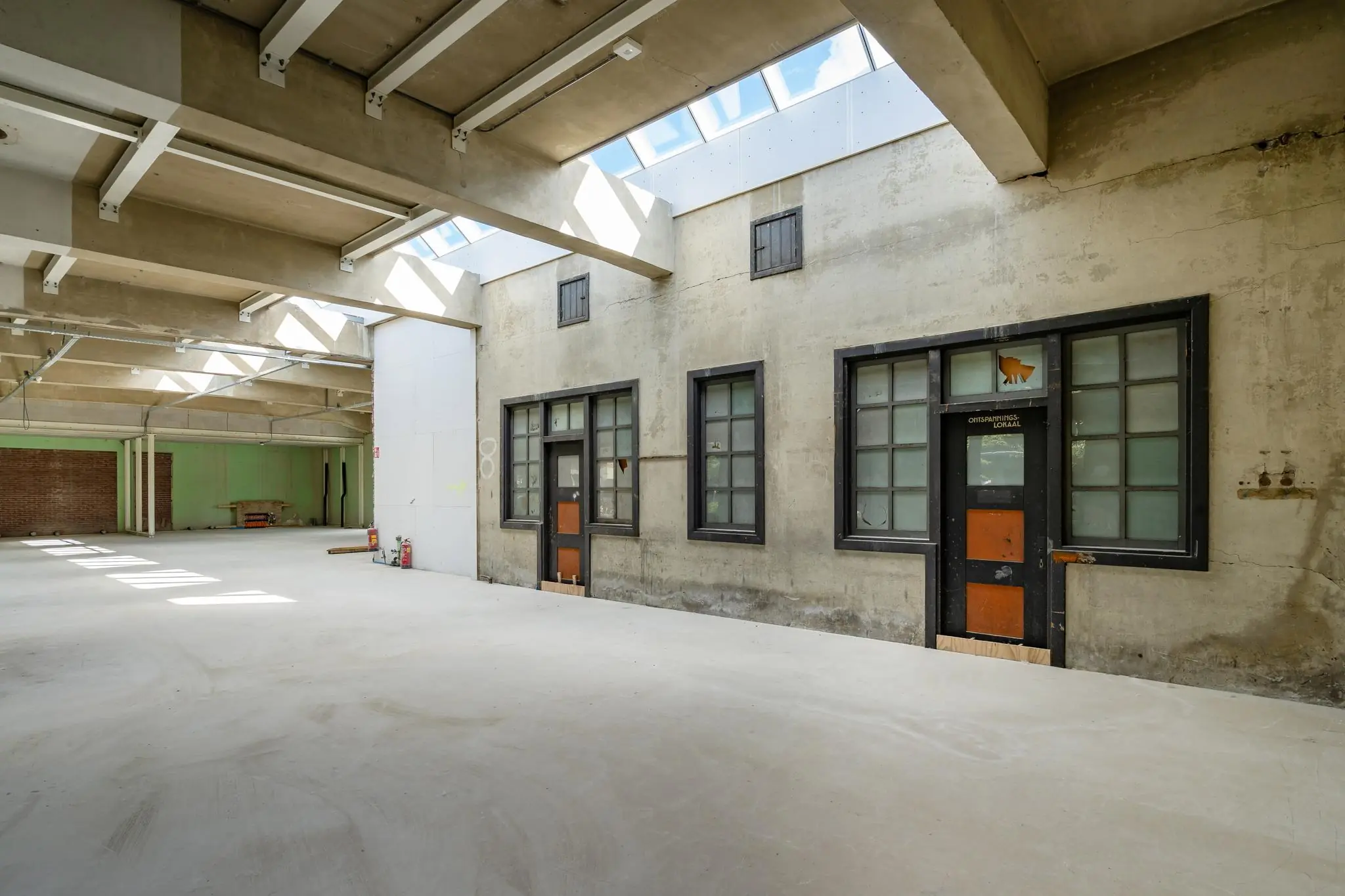 Licht industrieel gebouw met betonnen muren, hoge ramen en een oud lokaal met opschrift “Opleidingslokaal” aan het Stationsplein.