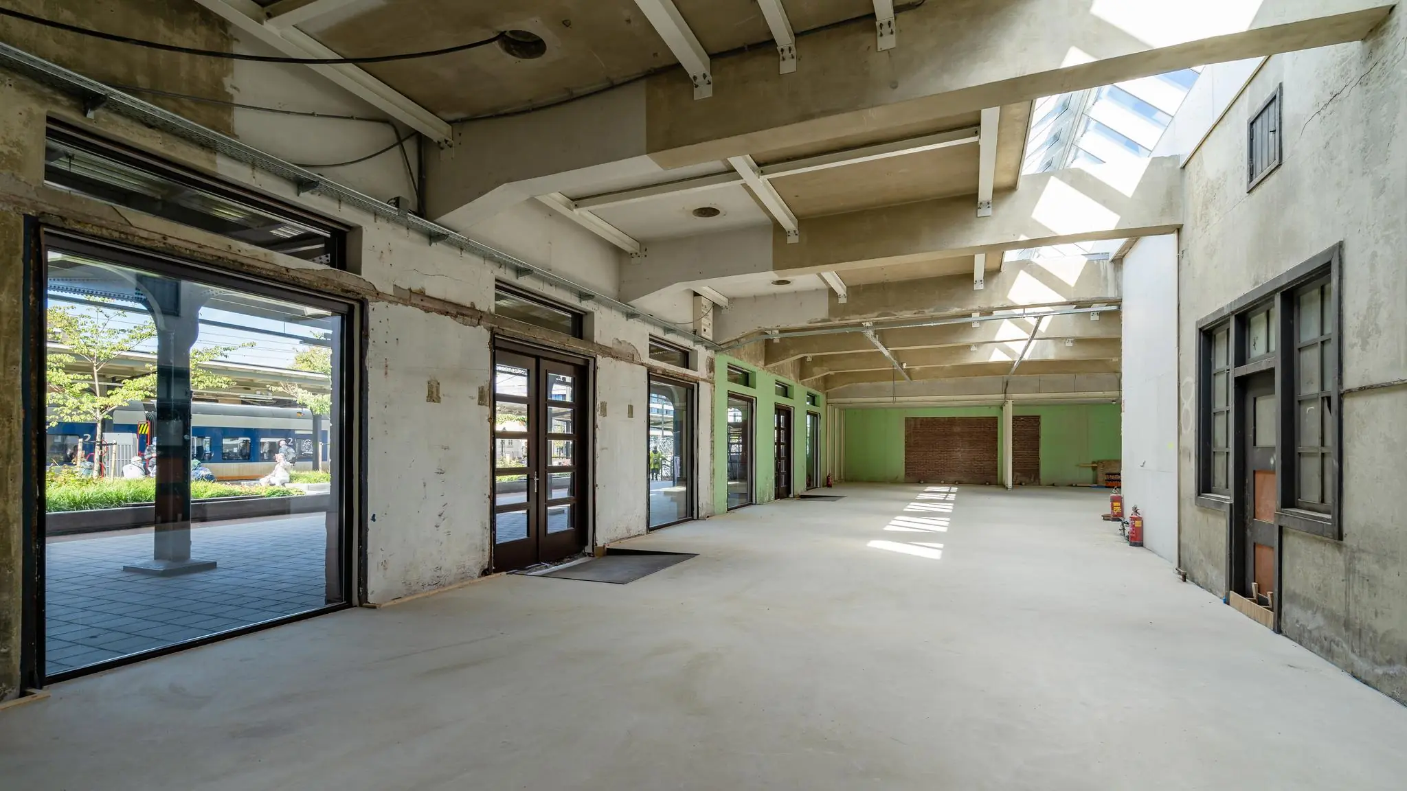 Leegstaand en deels gerenoveerd stationsgebouw aan het Stationsplein met uitzicht op het perron en een passerende trein.