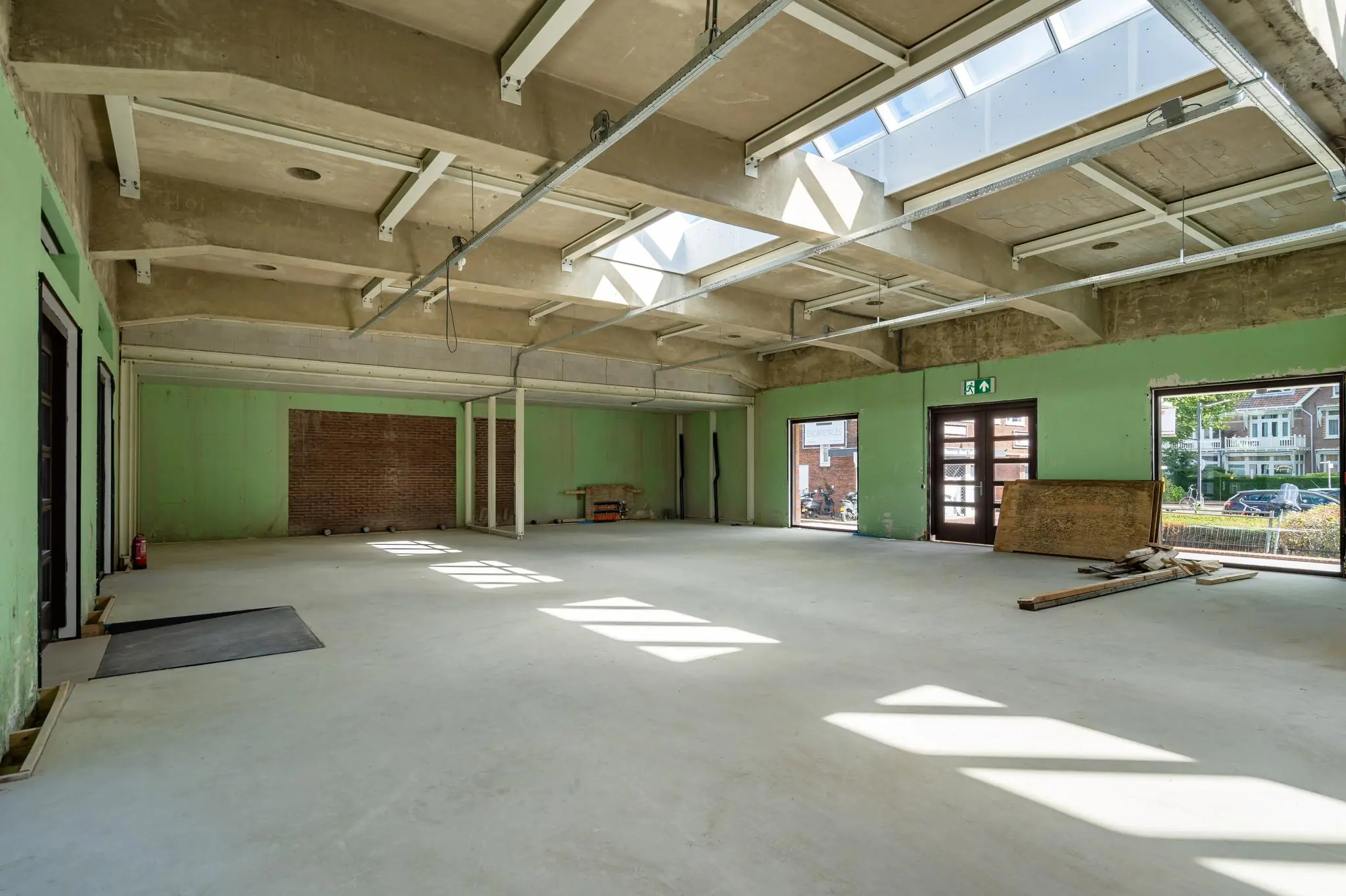 Leegstaand en grotendeels gerenoveerd interieur van een ruim pand aan het Stationsplein met betonnen plafond, dakramen en zicht op de straat.