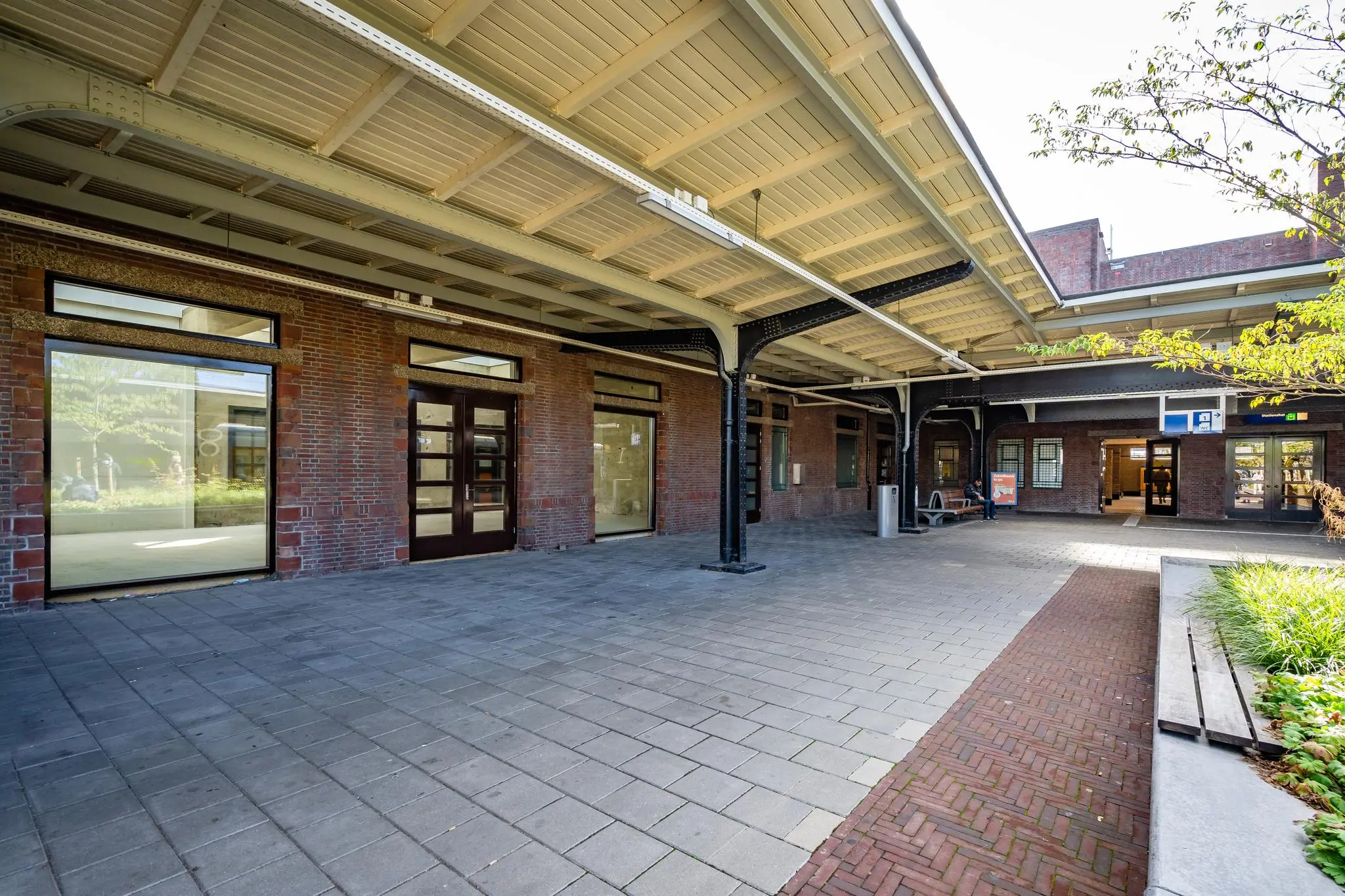 Overdekt stationsplein met bakstenen gevel, grote ramen en entree naar het station.
