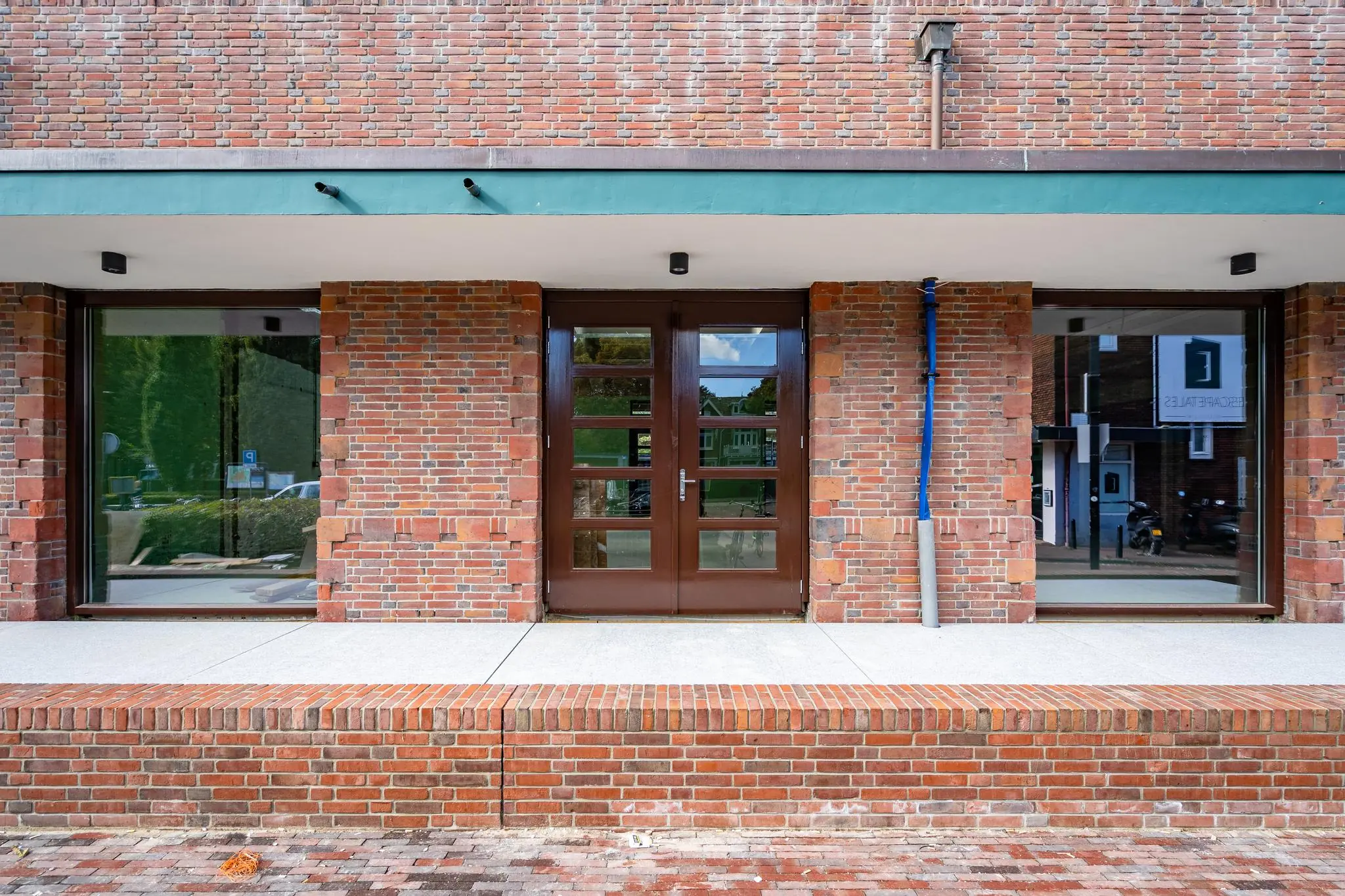 Ingang van een modern bakstenen gebouw aan het Stationsplein met glazen deuren en grote ramen.