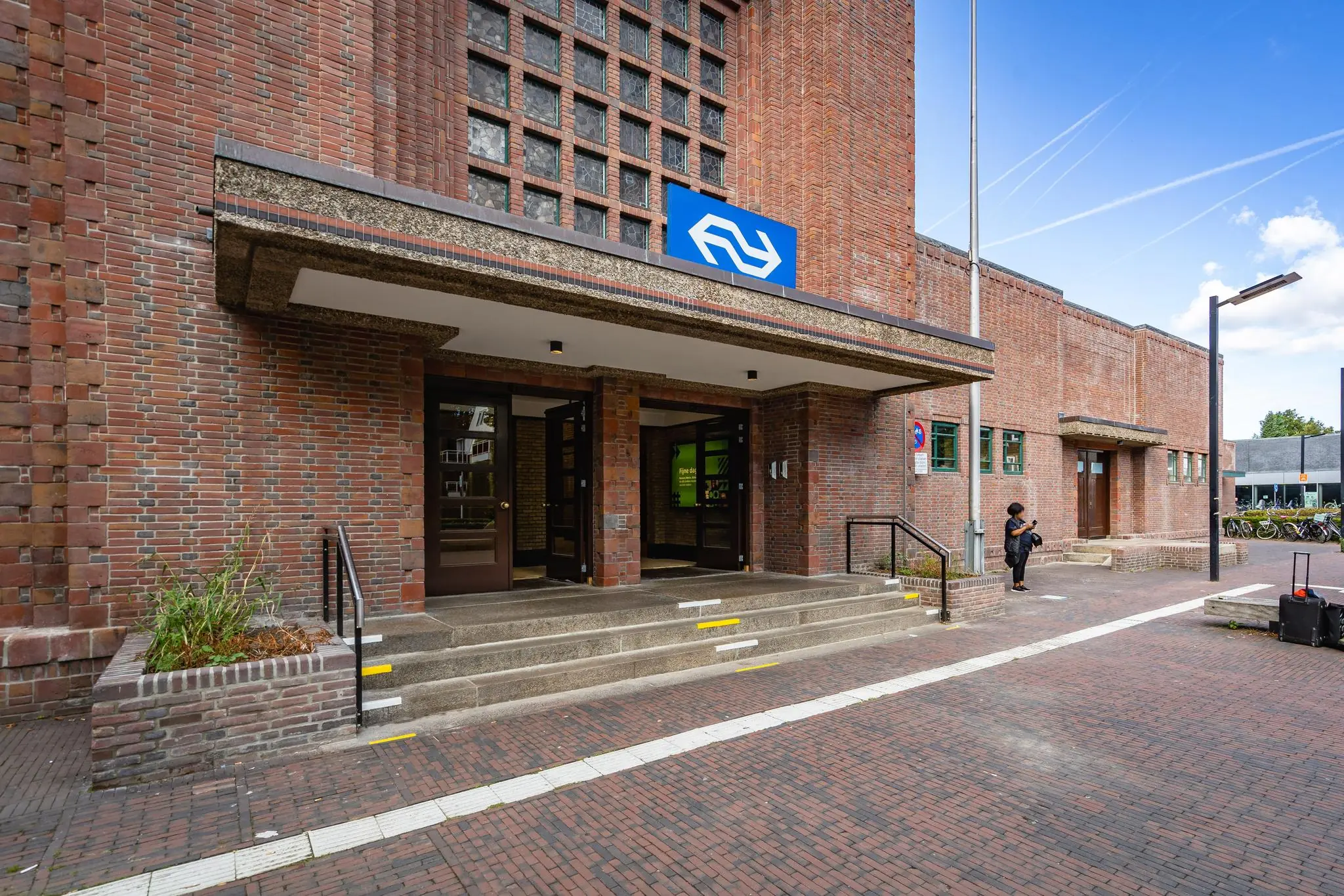 Ingang van een NS-station aan het Stationsplein met bakstenen gevel en trappen.