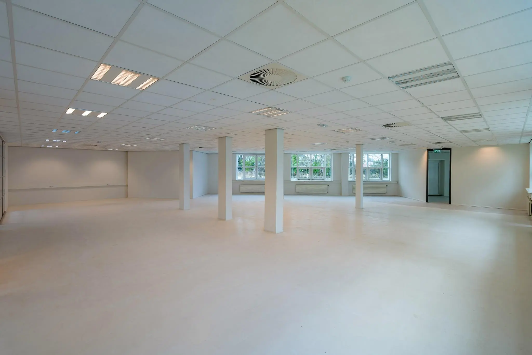 Lichte, lege kantoorruimte met witte muren, systeemplafond en ramen aan één zijde in het Rhijnspoorgebouw.