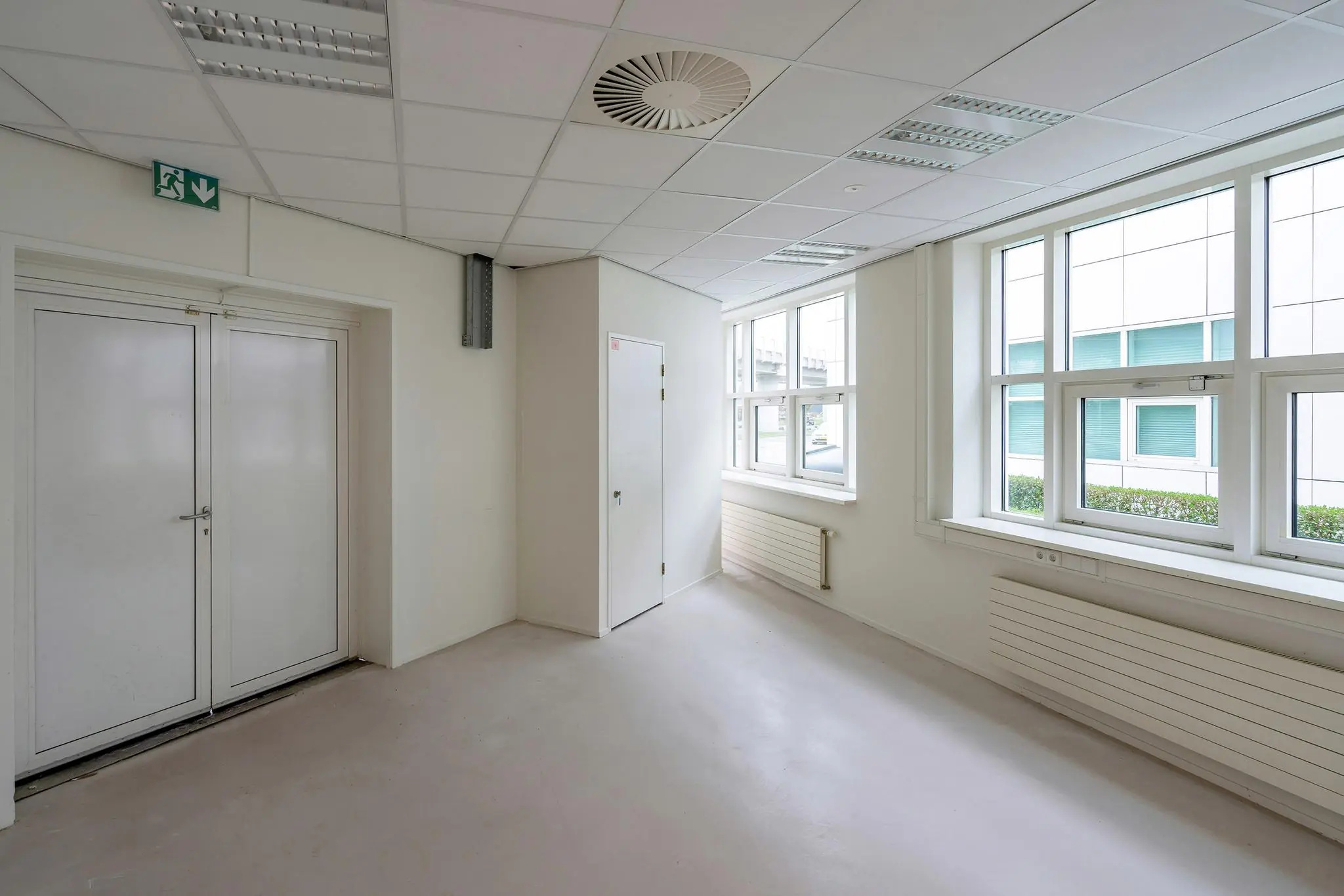 Leeg, wit kantoorruimte-interieur met dubbele deuren, ramen en radiatoren in het Rhijnspoorgebouw.