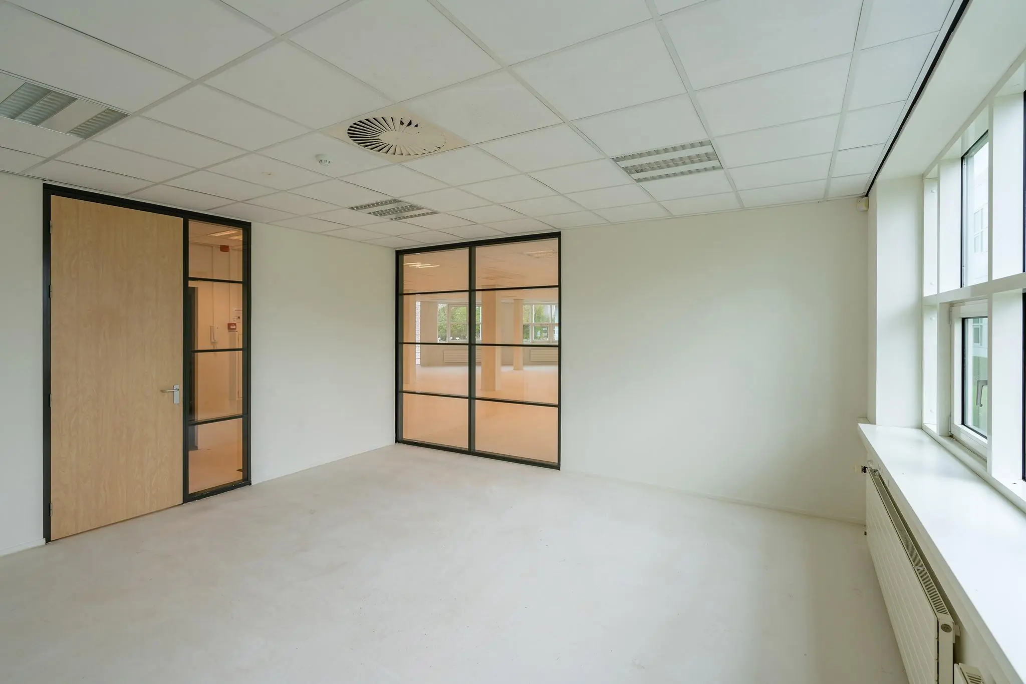 Lichte, lege kantoorruimte in het Rhijnspoor-gebouw met glazen binnenwanden en grote ramen.