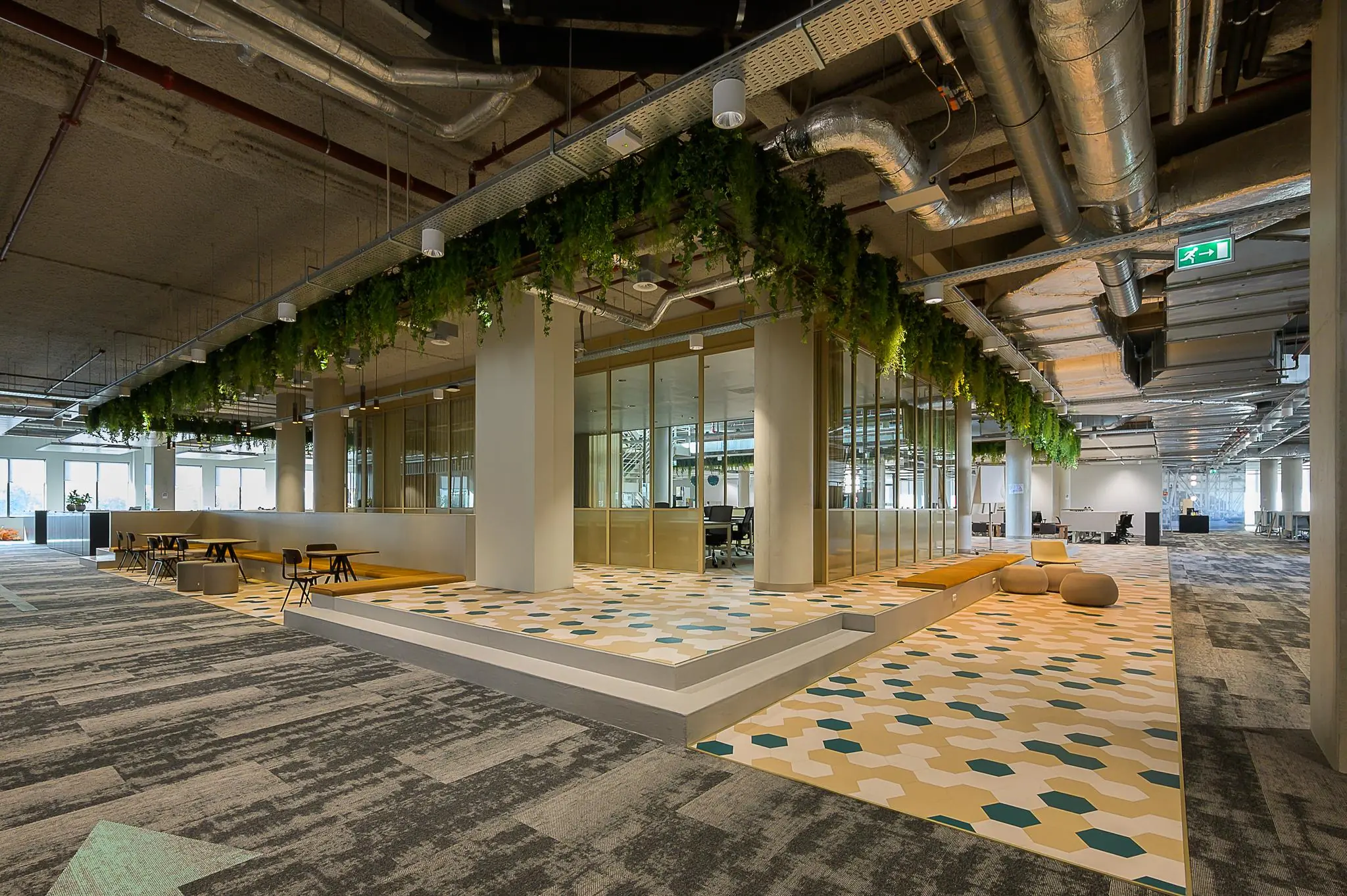 Moderne kantoorruimte aan de Coolsingel met open werkplekken, veel groen aan het plafond en geometrisch tegelpatroon op de vloer.