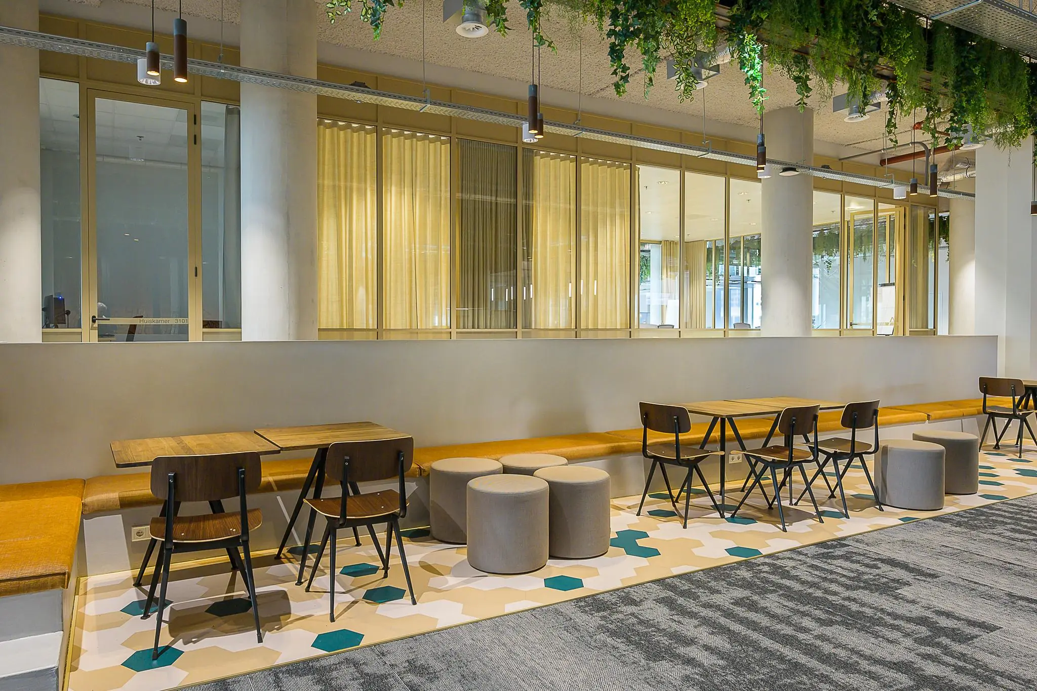 Moderne zitruimte aan de Coolsingel met houten tafels, stoelen, poefjes en hangende planten aan het plafond.