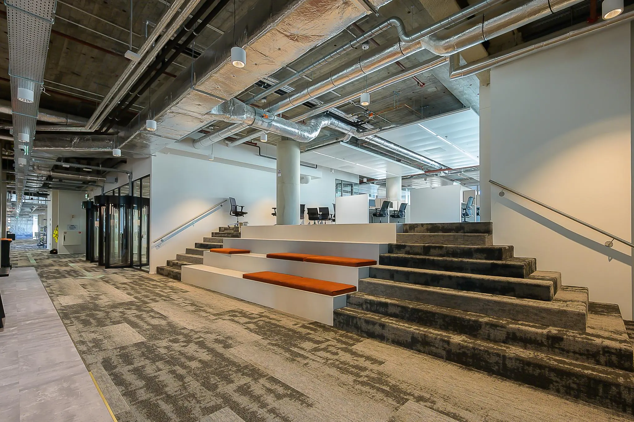 Moderne kantoorruimte aan de Coolsingel met open werkplekken, industriële plafonds en een tribune met zitkussens.