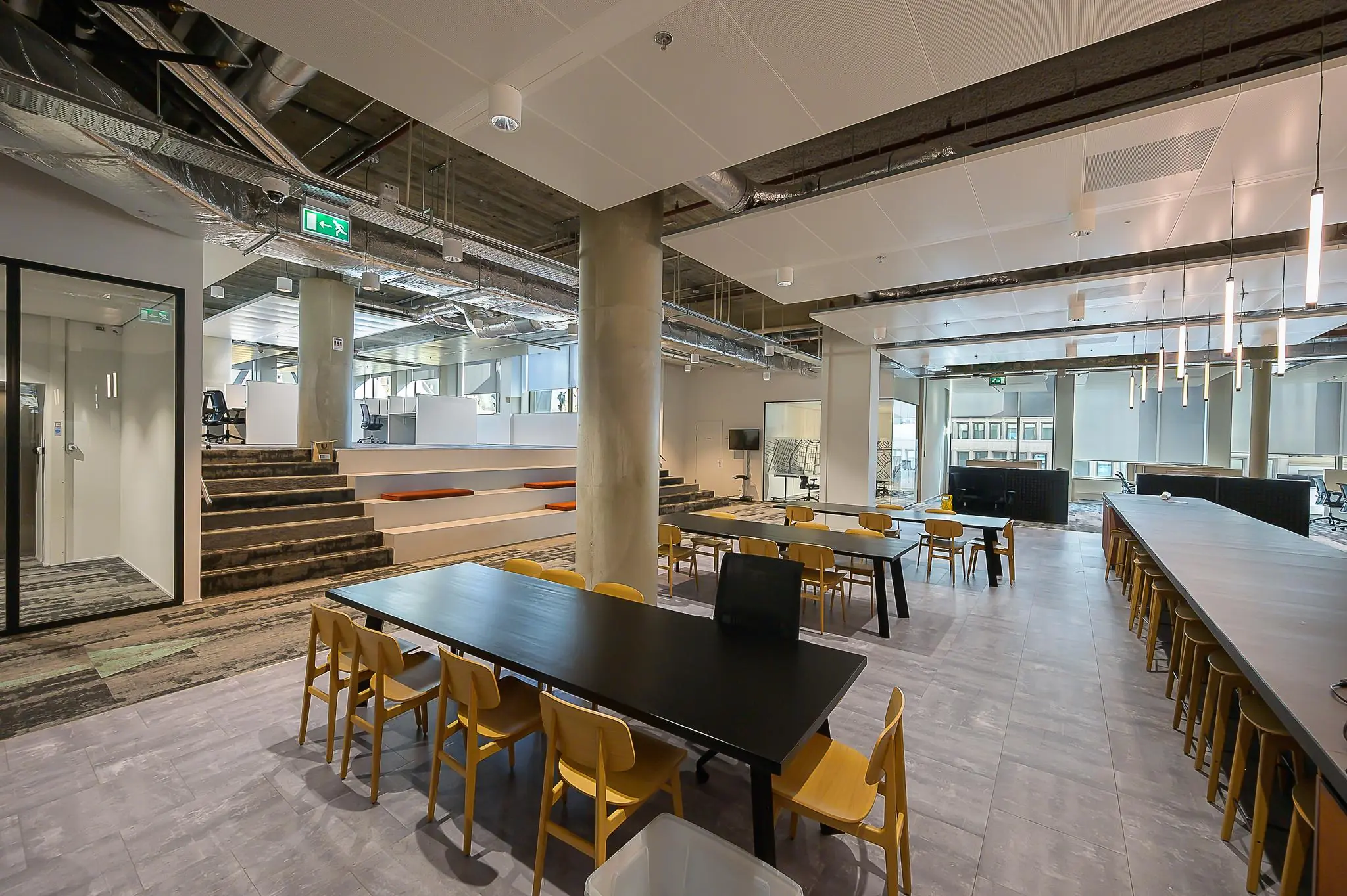 Moderne en open kantoorruimte aan de Coolsingel met lange werktafels, tribunezitjes en industriële plafonduitwerking.