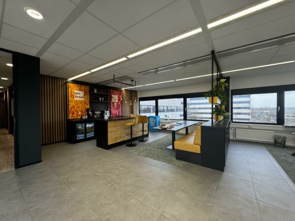 Moderne kantoorruimte in Rijnzathe met koffiecorner, zitgedeelte en uitzicht op kantoorgebouwen.